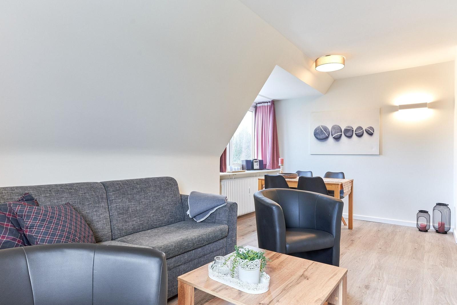 Wohnzimmer mit Sofa, Sessel und Esstisch. Dachgeschoss mit Holzboden und Fenster.