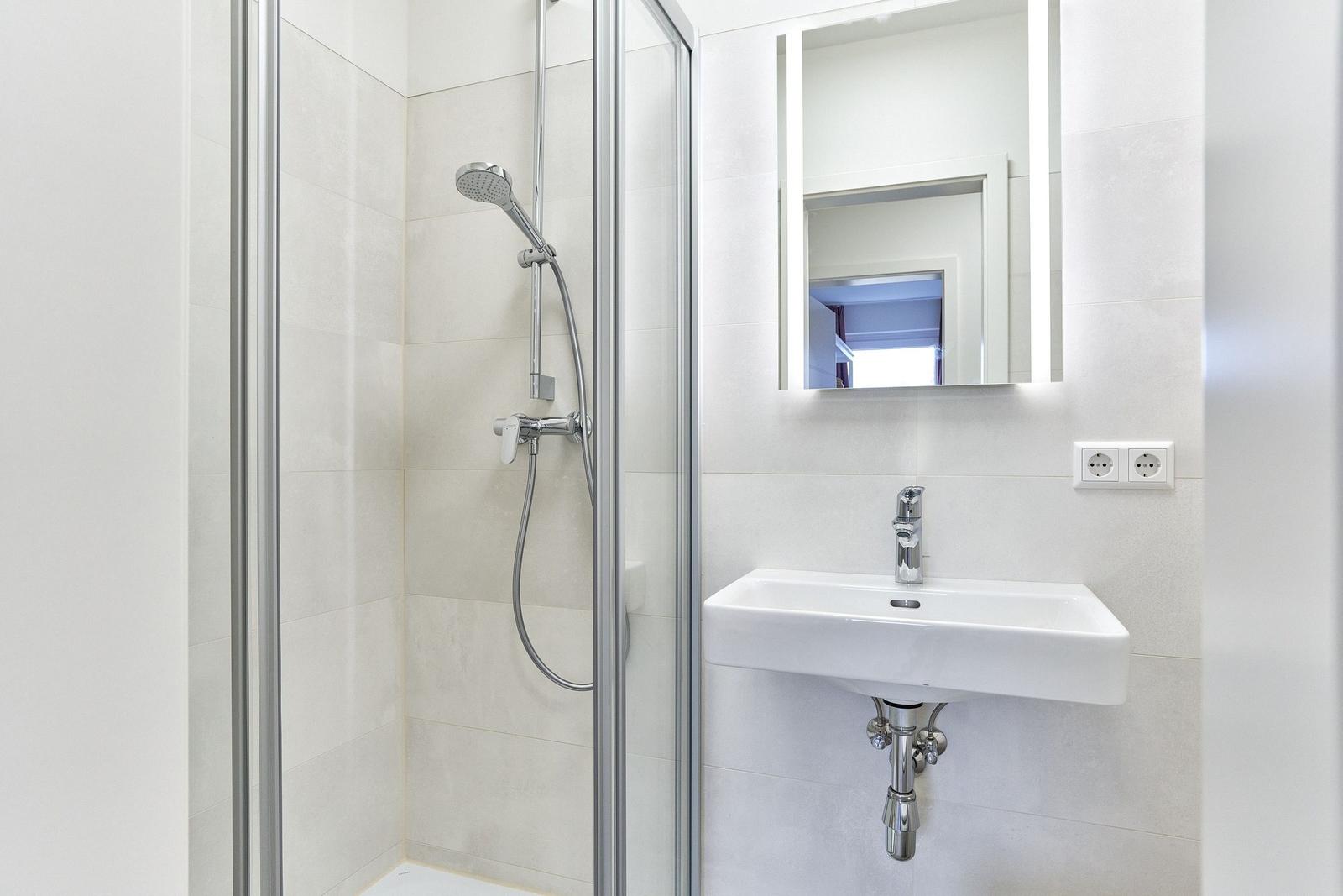Badezimmer mit Dusche, Waschbecken und beleuchtetem Spiegel.