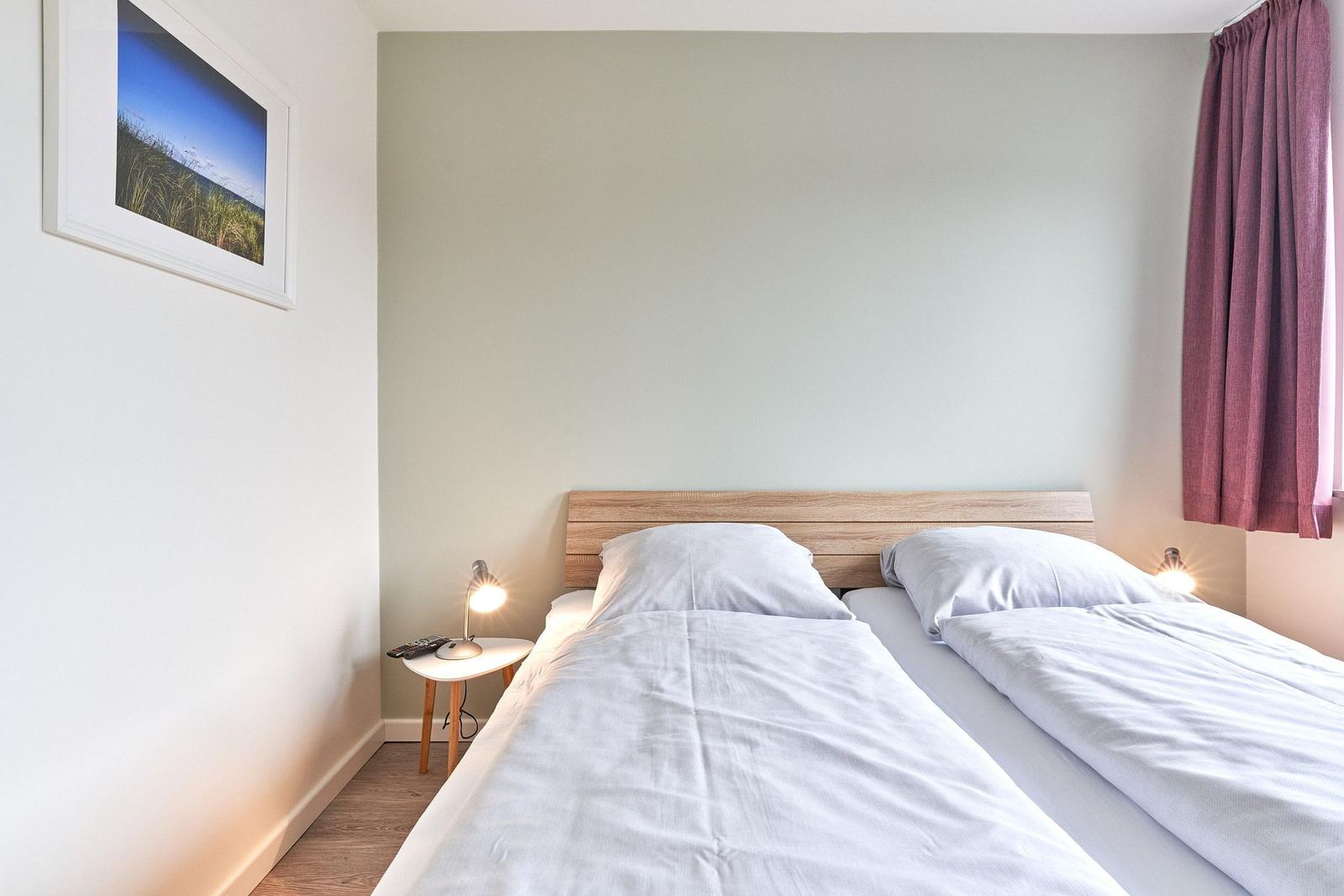 Zwei Betten mit weißen Bettwäschen, Nachttisch mit Lampe und Wandbild.