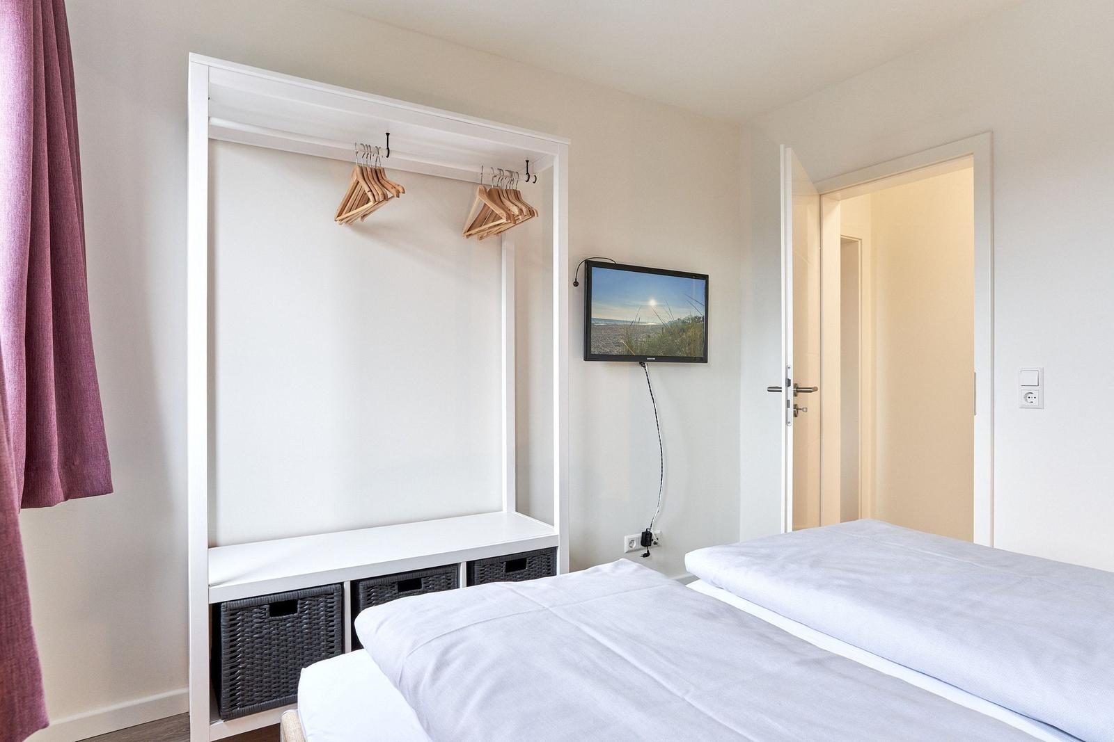 Zwei Betten, Kleiderschrank mit Haken und Fernseher an der Wand.