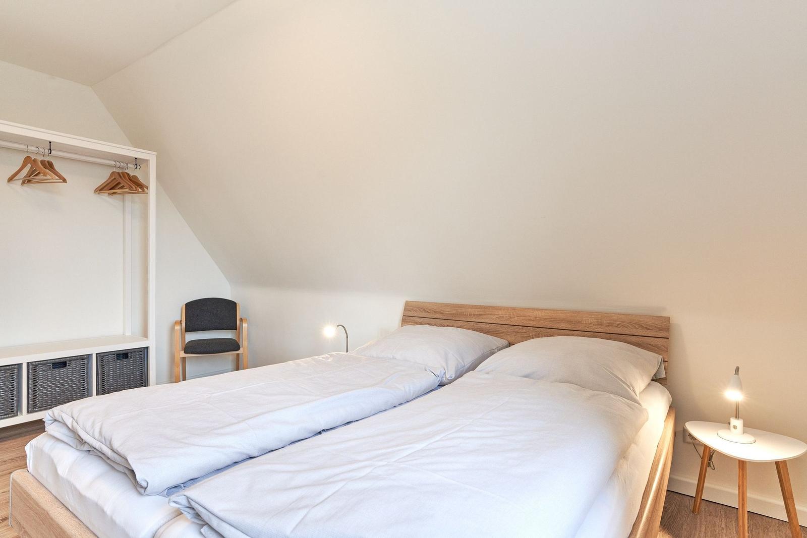 Doppelbett mit Holzrahmen, Nachttisch und Kleiderschrank unter Dachschrägen.
