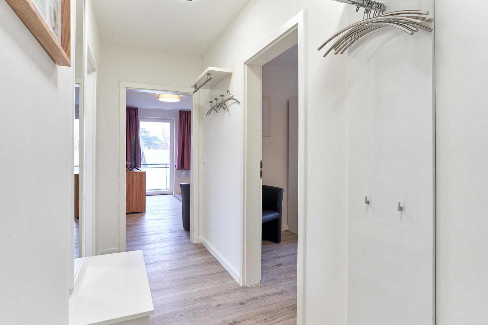 Flur mit Kleiderständer, Tür zu Wohnzimmer und Schlafzimmer, Holzboden und weißer Wand