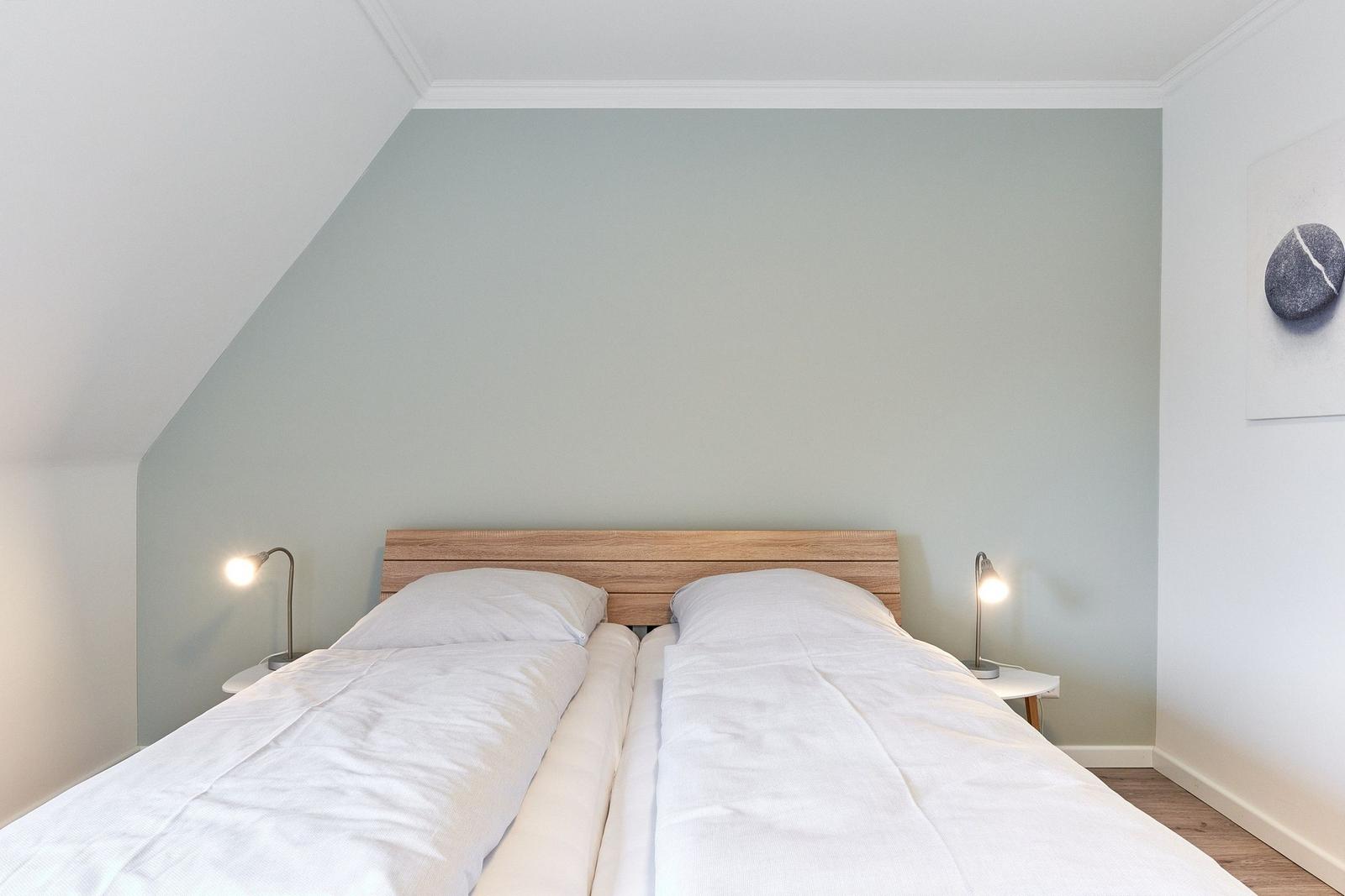 Zimmer mit Doppelbett, Holzkopfteil und zwei Nachttischen mit Lampen.