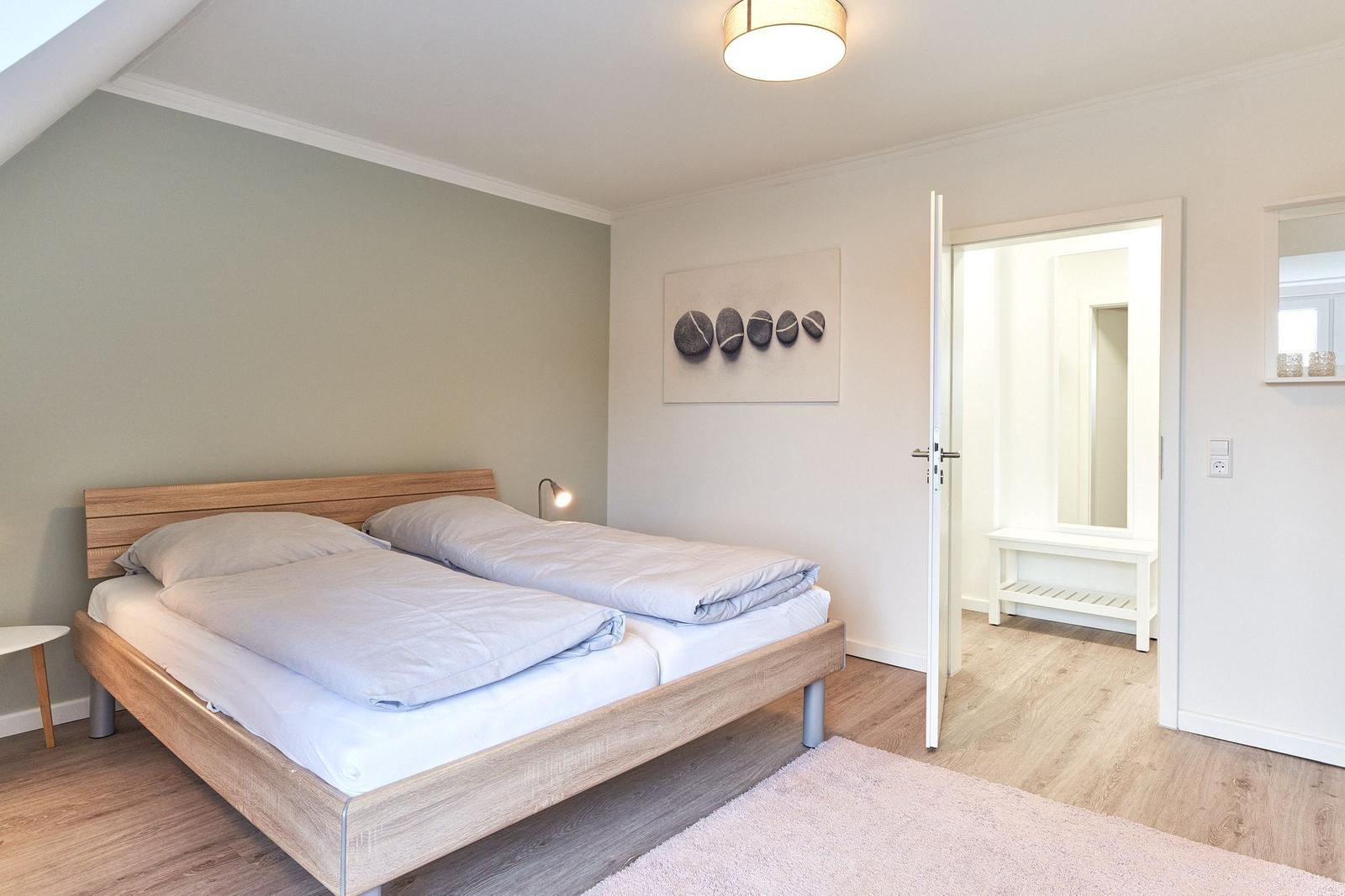 Schlafzimmer mit Doppelbett, Holzboden und Wandbild mit Steinen.