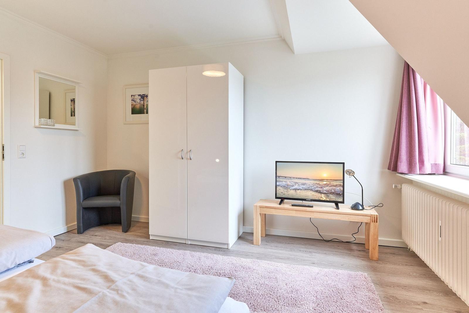 Schlafzimmer mit Bett, Kleiderschrank, Sessel und TV auf Holztisch.
