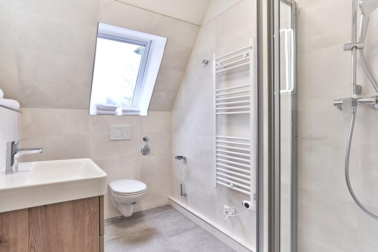 Badezimmer mit Dusche, Toilette und Waschbecken unter Dachschrägen.