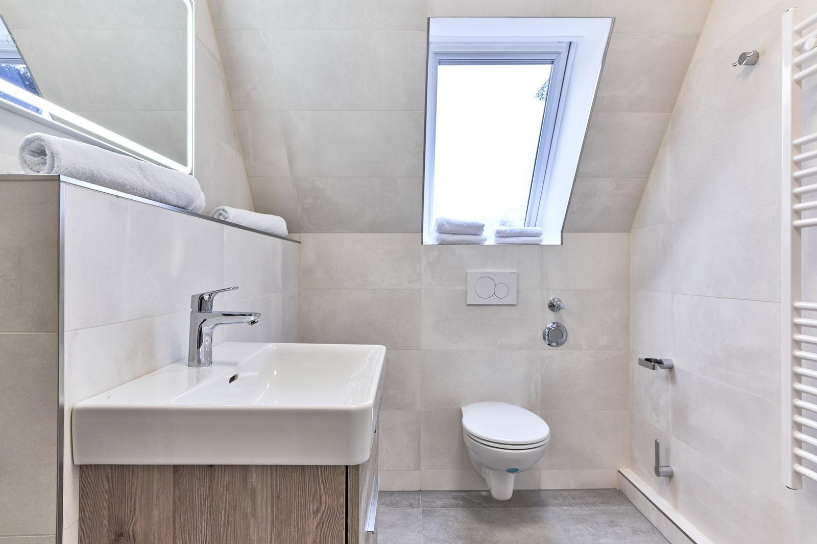Badezimmer mit Waschbecken, Toilette und Dachfenster. Fliesenwand und Heizkörper.