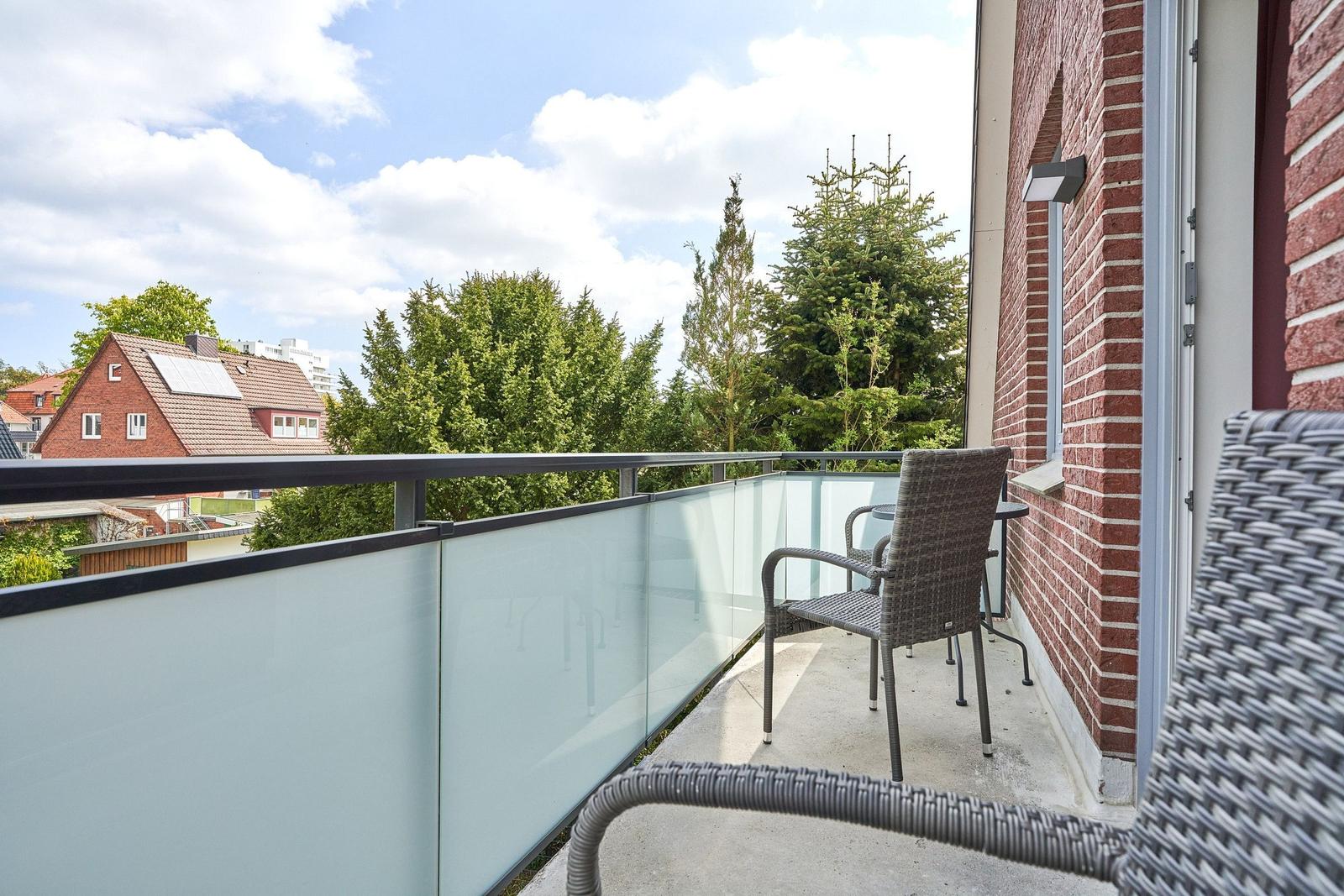 Balcony with glass railing, wicker chairs, and view of trees and houses.
