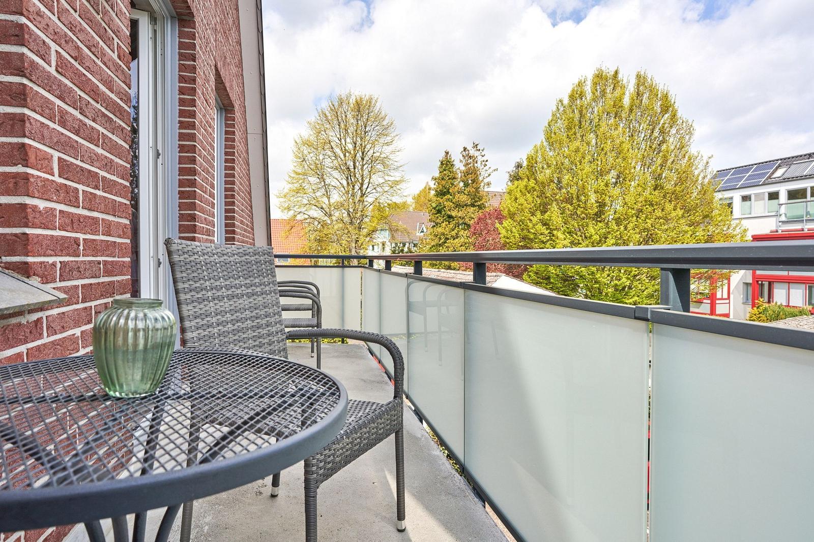 Terrasse mit Tisch, Stühlen und Glasgeländer. Blick auf Bäume und Nachbarhäuser.