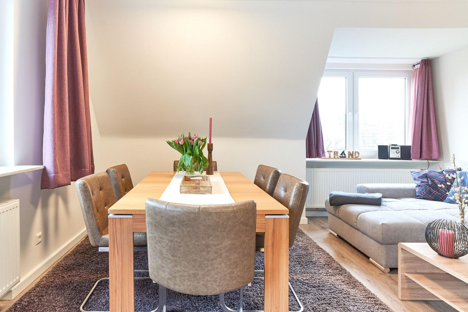 Essbereich mit Holztisch und Stühlen, daneben Wohnbereich mit Sofa und Fenster.