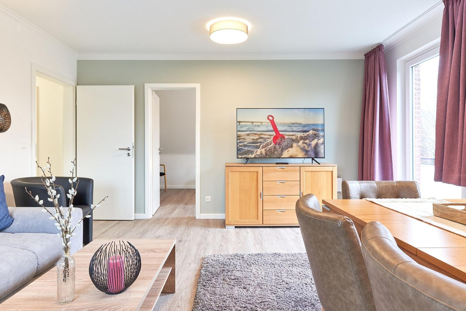 Wohn- und Essbereich mit TV, Holzmöbeln und Fenster mit Vorhängen.