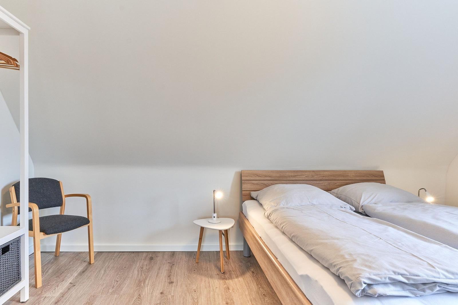 Schlafzimmer mit Doppelbett, Nachttisch und Stuhl. Holzboden und weiße Wände.