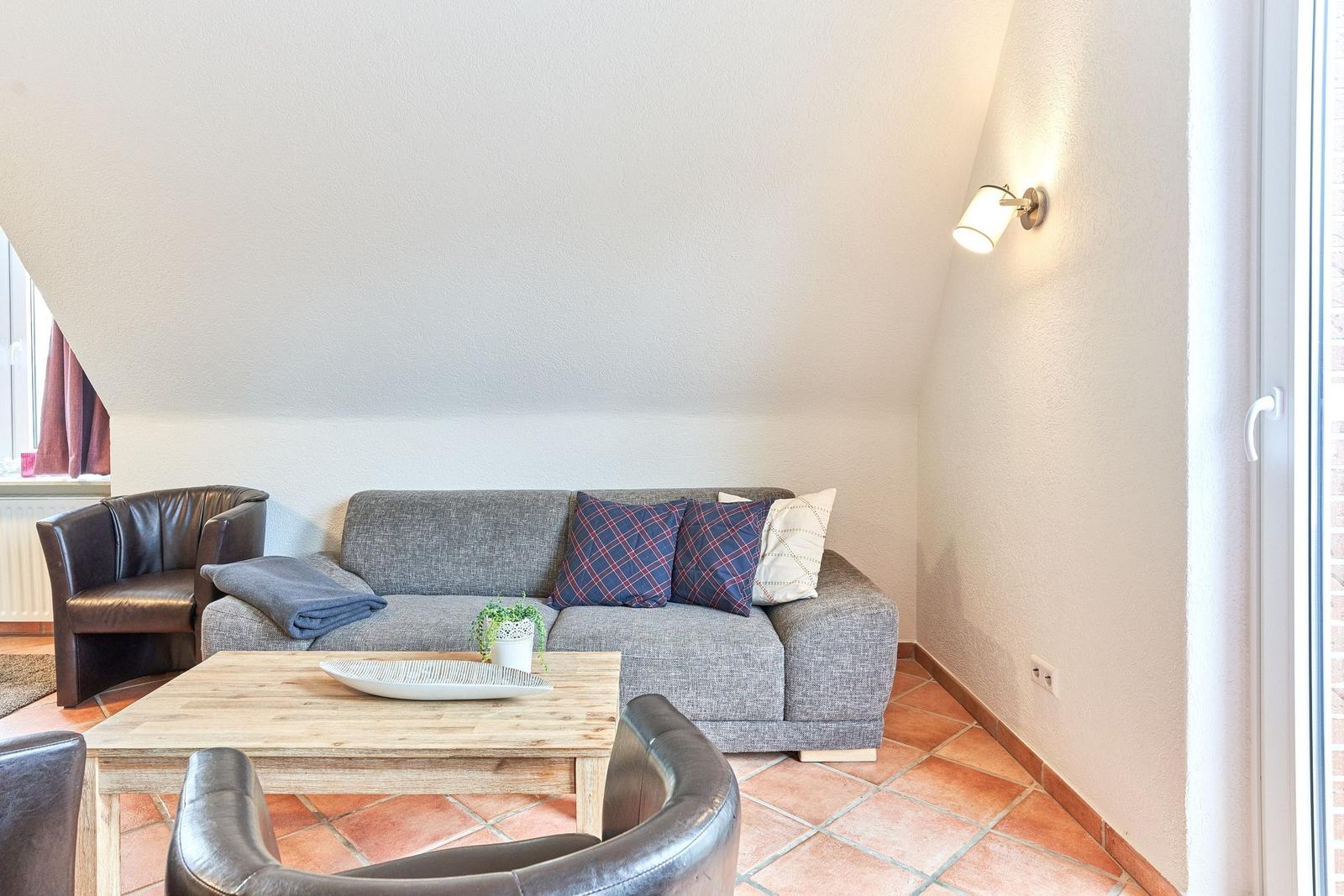 Wohnzimmer mit Sofa, Sessel und Holztisch. Terrakottafußboden und schräge Decke.