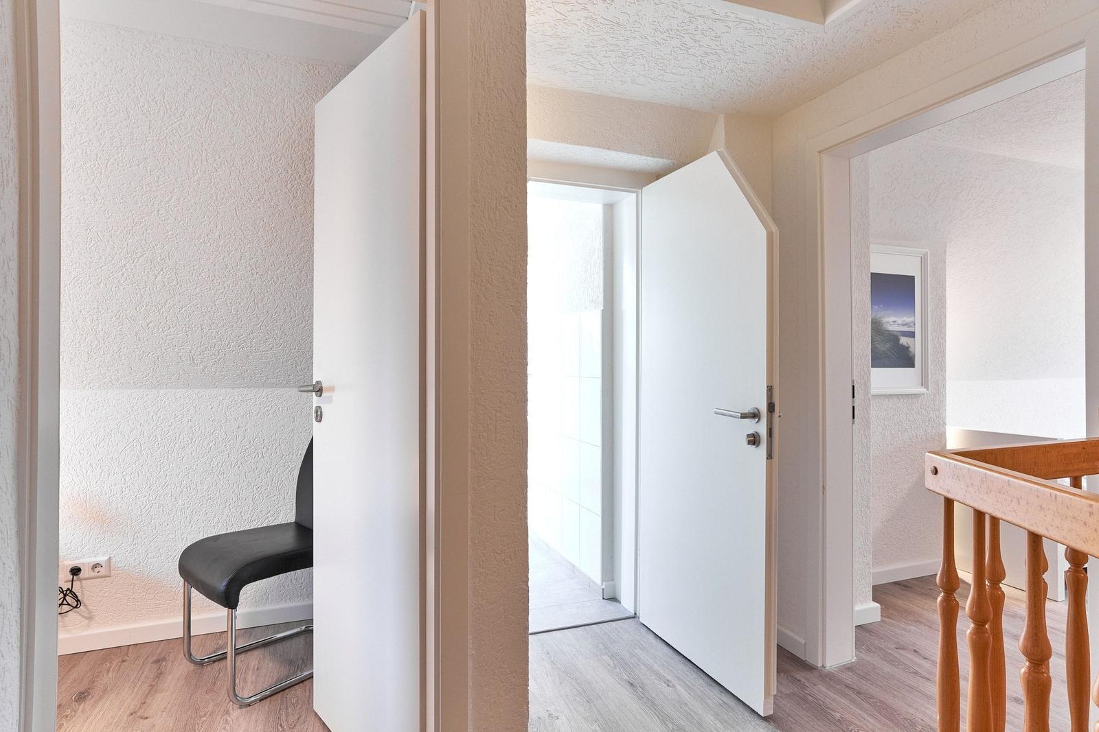 Flur mit Türen und Stuhl. Holzgeländer und Wandbild sichtbar.