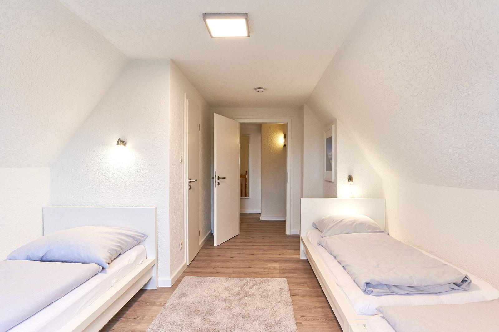 Zwei Einzelbetten in einem Dachgeschosszimmer mit Holzboden und Stehlampe.