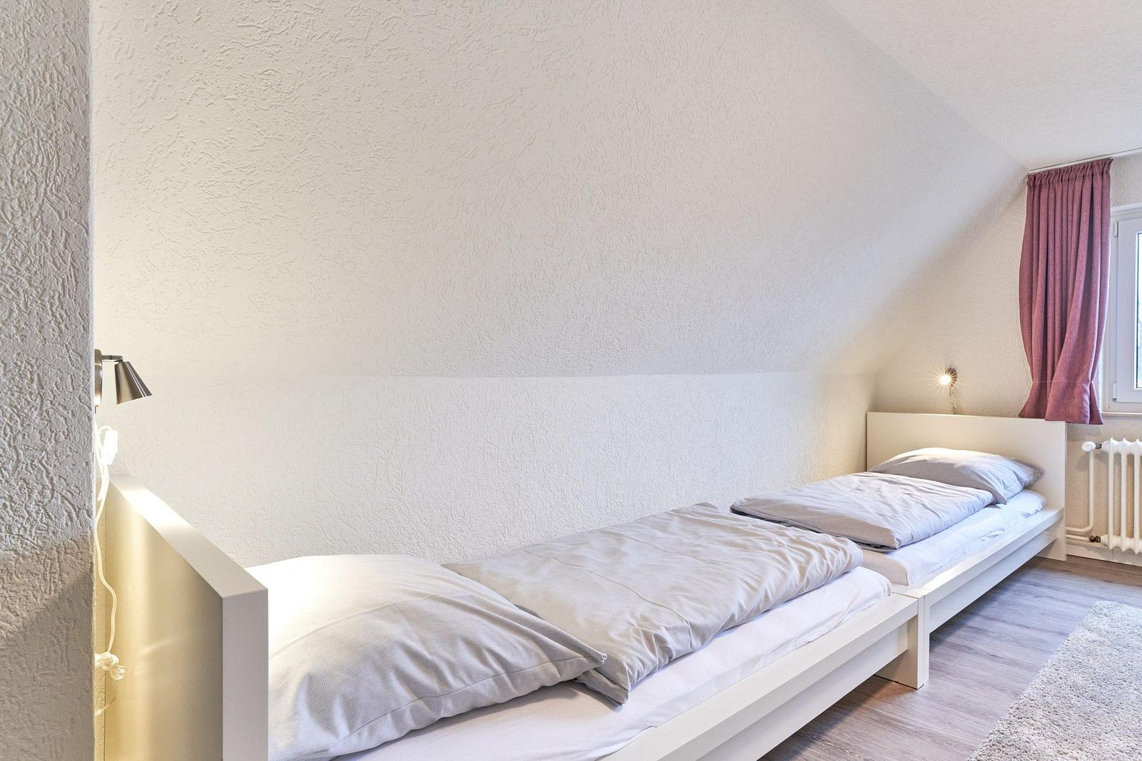 Zwei Betten in einem Schlafzimmer mit Dachschräge und Fenster mit Vorhang.