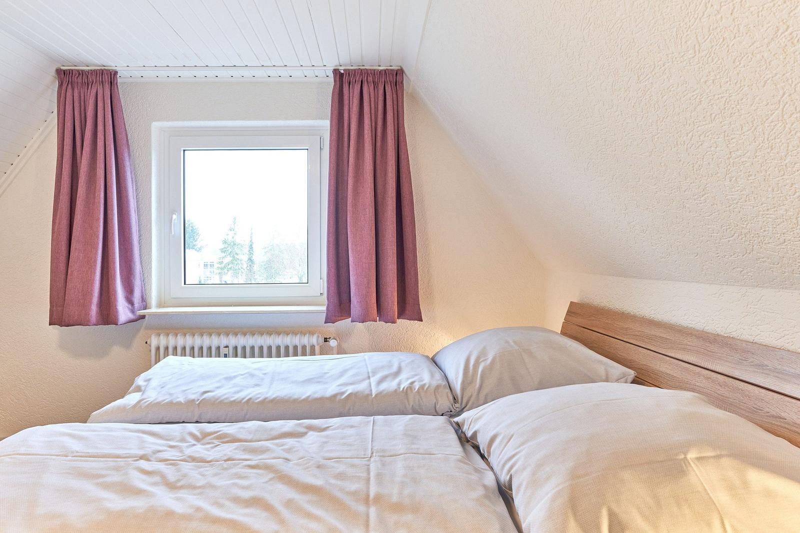 Schlafzimmer mit Doppelbett, Fenster und rosa Vorhängen.