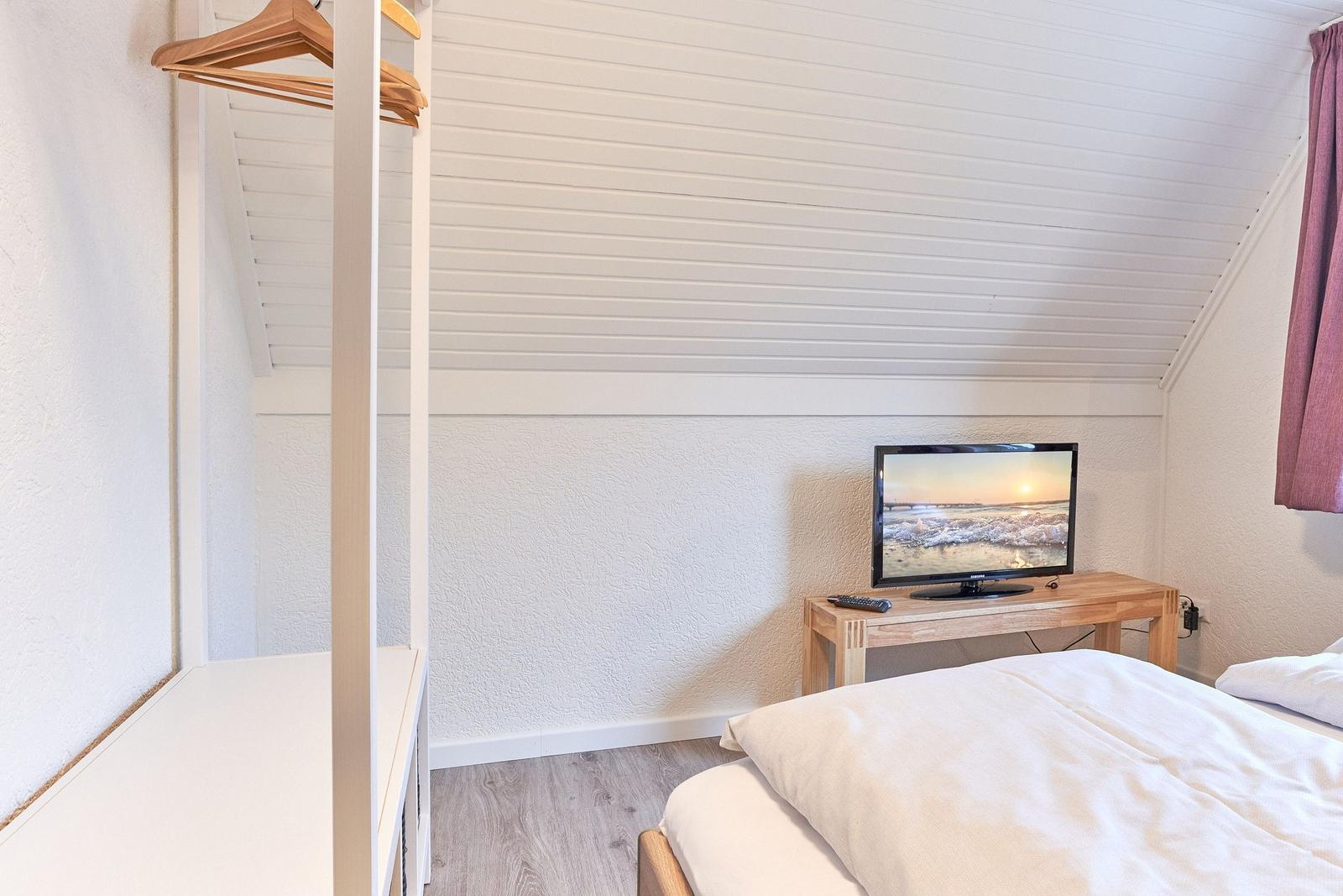 Schlafzimmer mit Bett, Kleiderständer und Fernseher auf Holztisch.