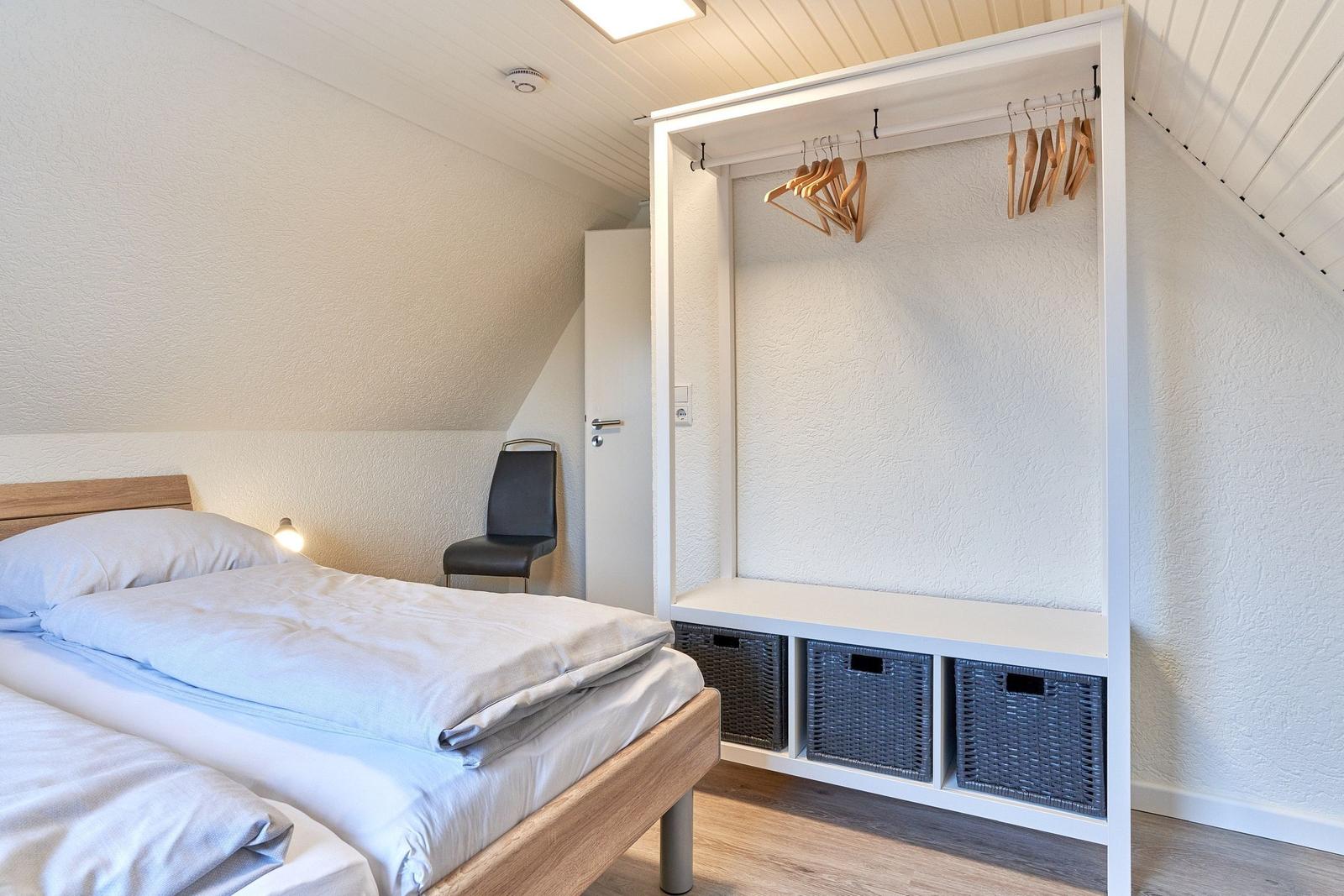 Schlafzimmer mit Bett, Kleiderschrank und Stuhl unter schrägen Dachdecken.