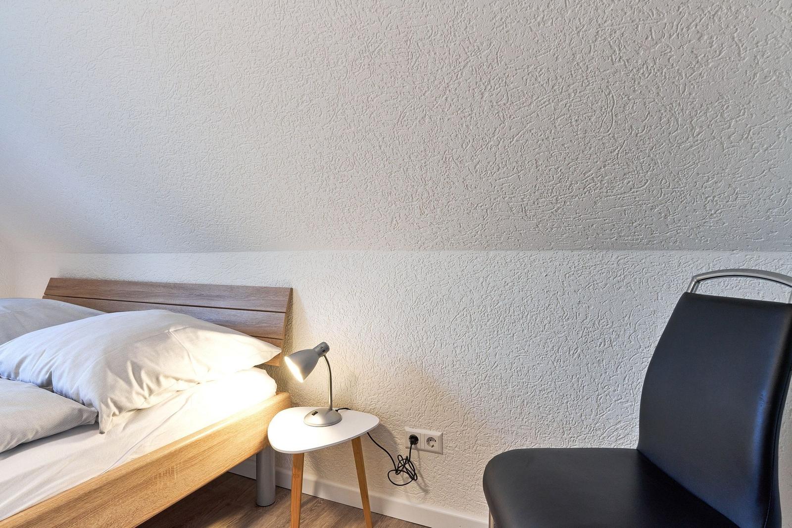 Schlafzimmer mit Bett, Nachttisch und Stuhl. Wand mit strukturiertem Putz.