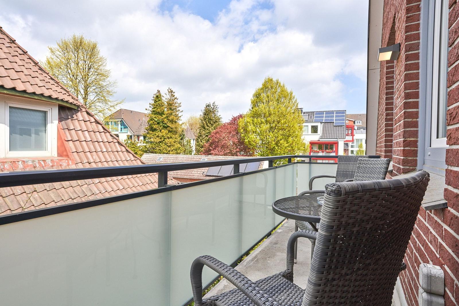 Terrasse mit Tisch und Stühlen, Blick auf Dächer und Bäume.