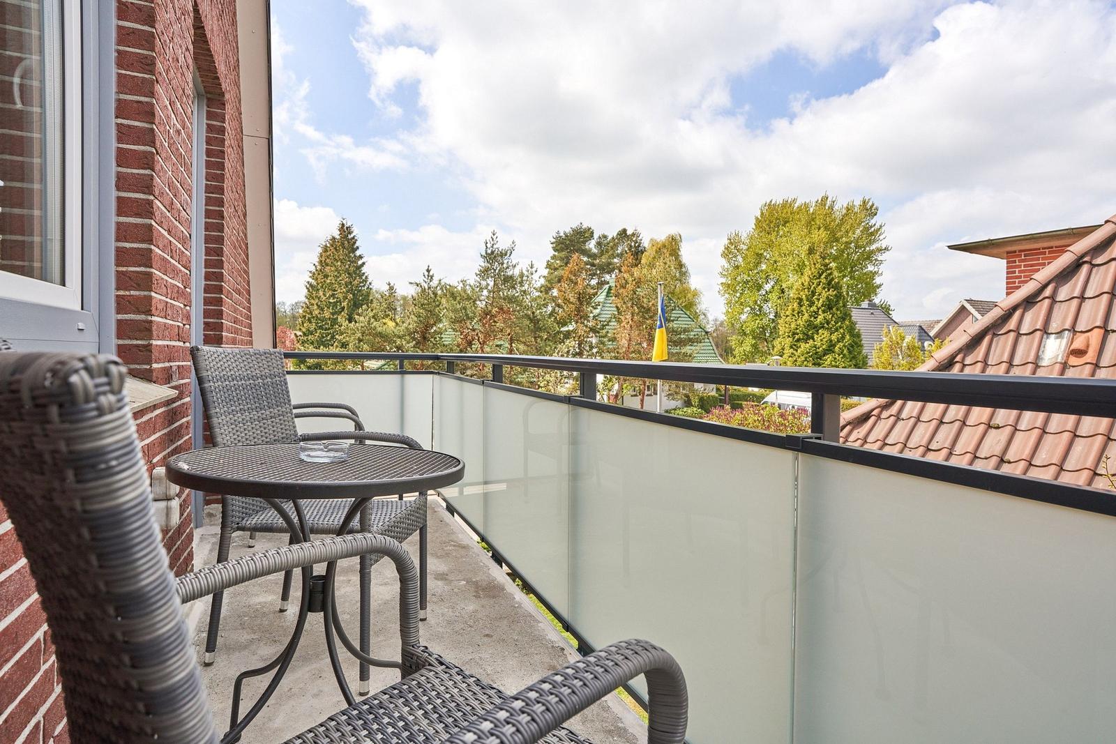 Balkon mit Tisch und Stühlen, Blick auf Bäume und Dächer.
