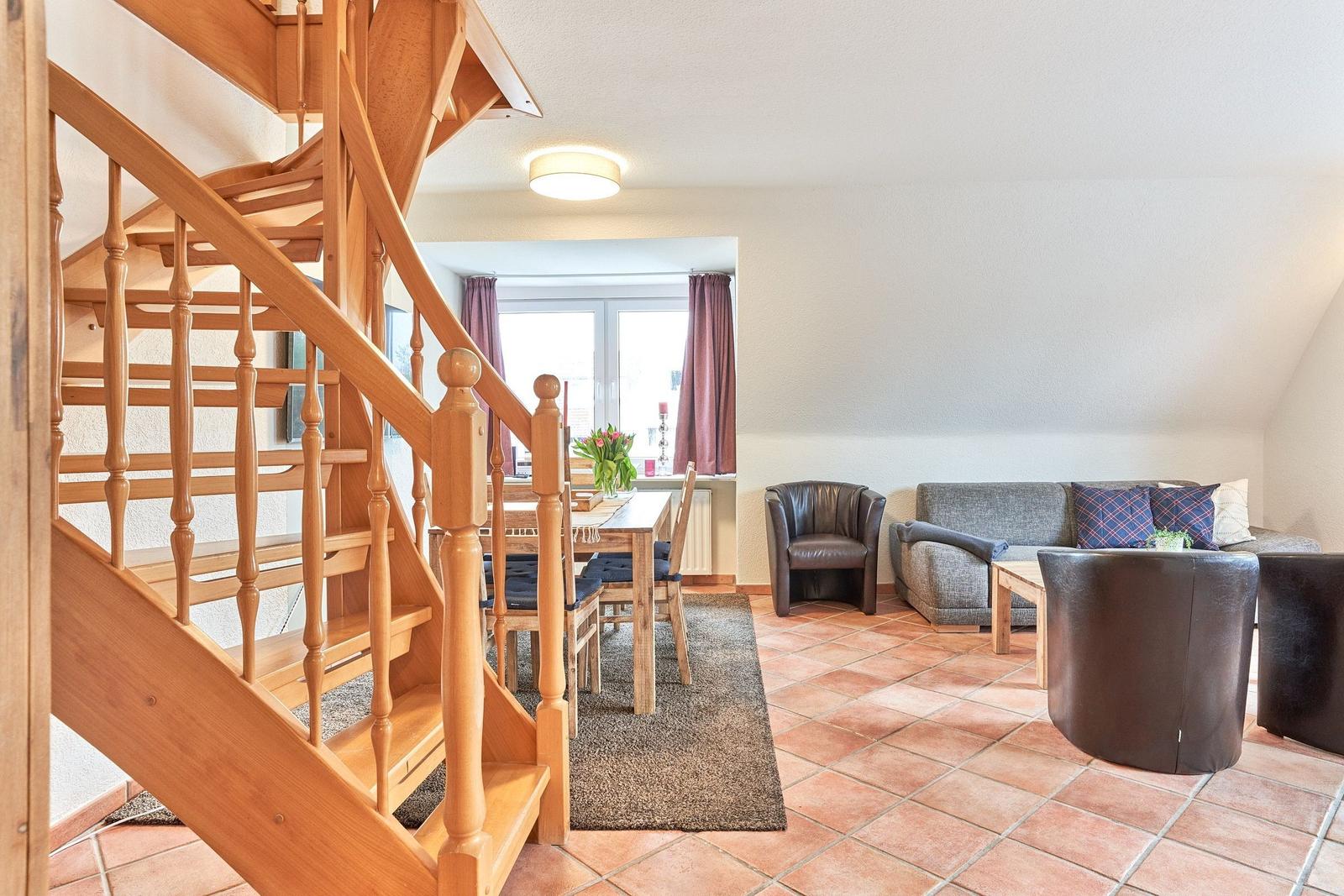 Eingangsbereich mit Holztreppe, Essbereich und Wohnzimmer mit Sofa und Sesseln.