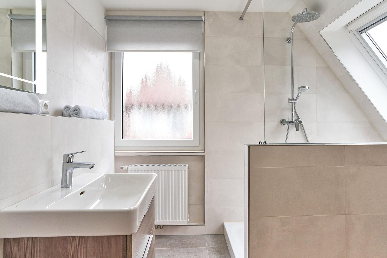 Badezimmer mit Dusche, Waschbecken und Fenster mit Rollladen.
