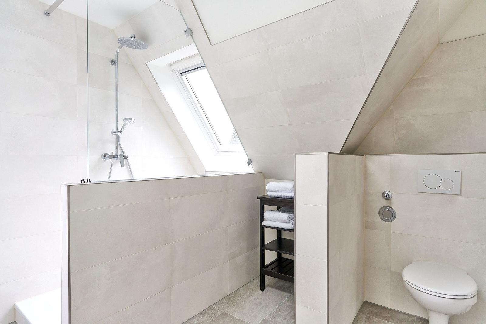 Dusche mit Dachfenster, Toilette und Handtuchständer in hellen Fliesen.