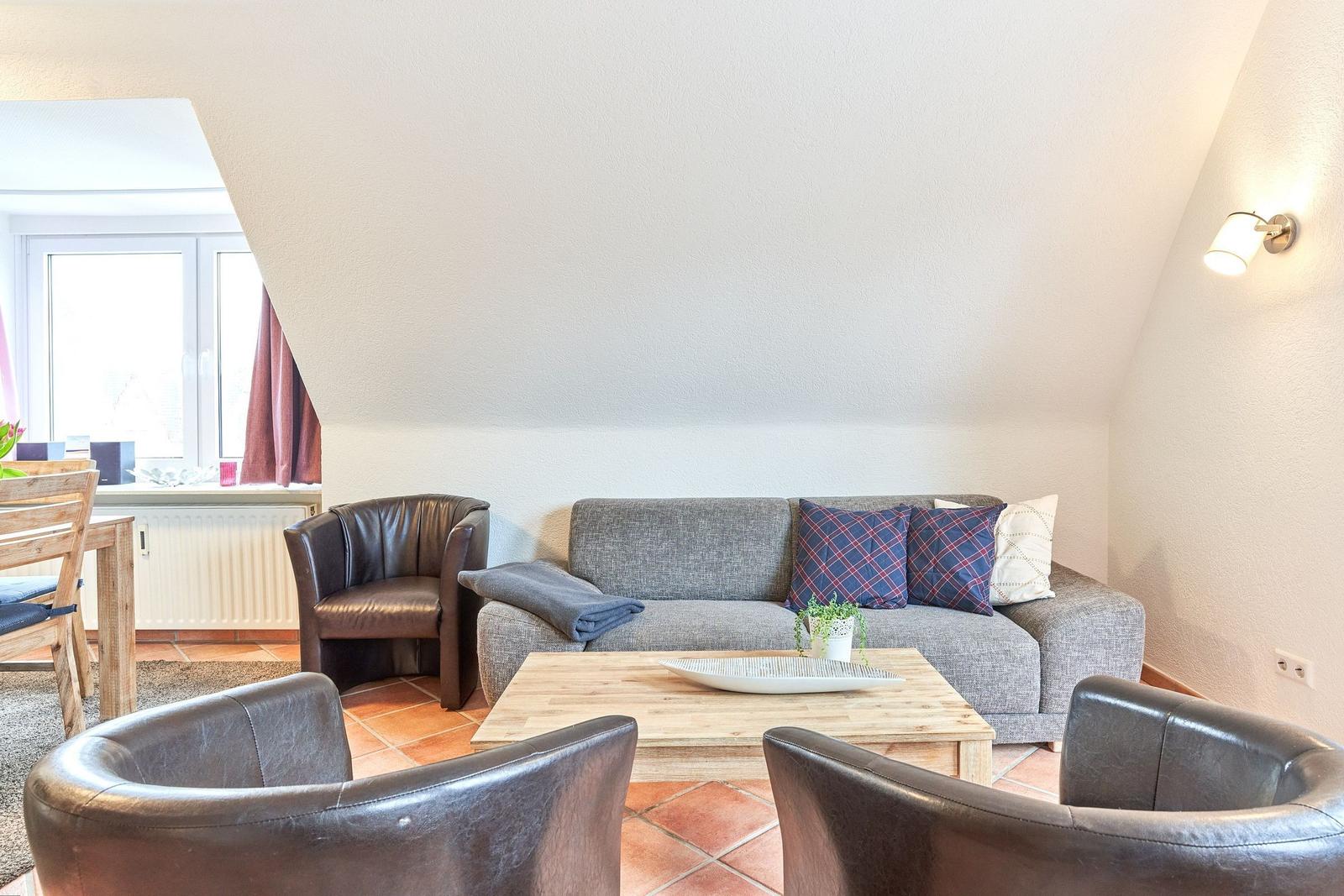 Wohnzimmer mit Sofa, zwei Ledersesseln und Holztisch unter schrägem Dach.