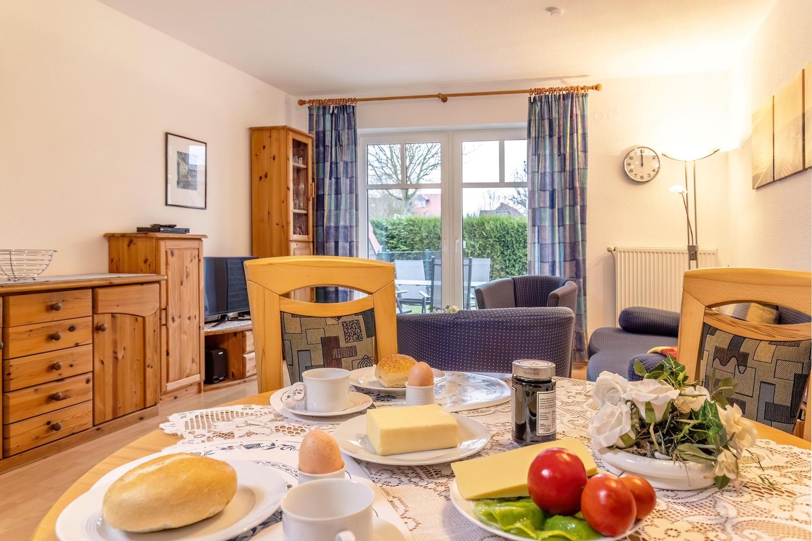 Frühstückstablett mit Käse, Eiern und Obst auf Tisch. Im Hintergrund Wohnzimmer mit Sitzgruppe und Balkon.