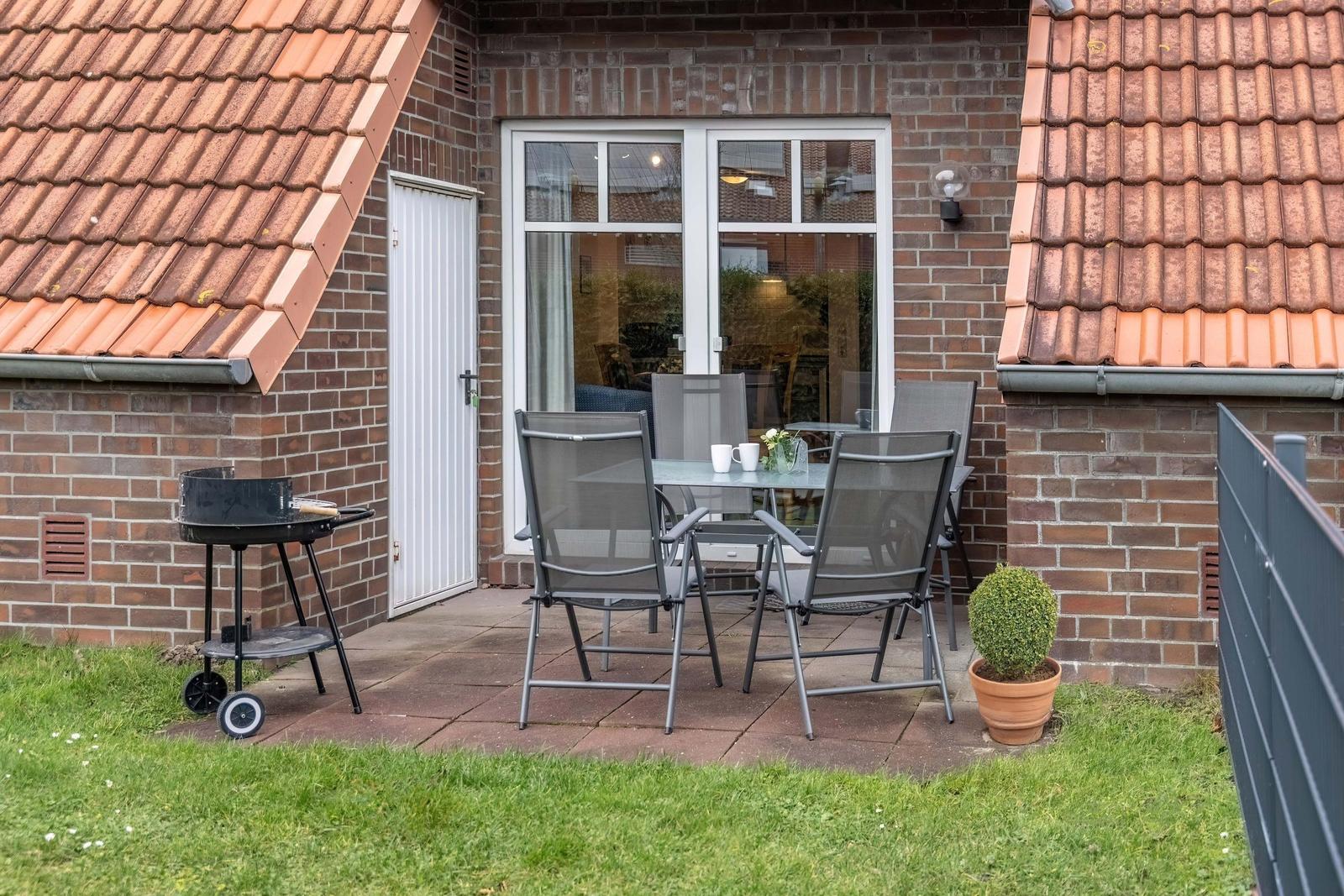 Terrasse mit Tisch, Stühlen, Grill und Pflanze vor Backsteinhaus