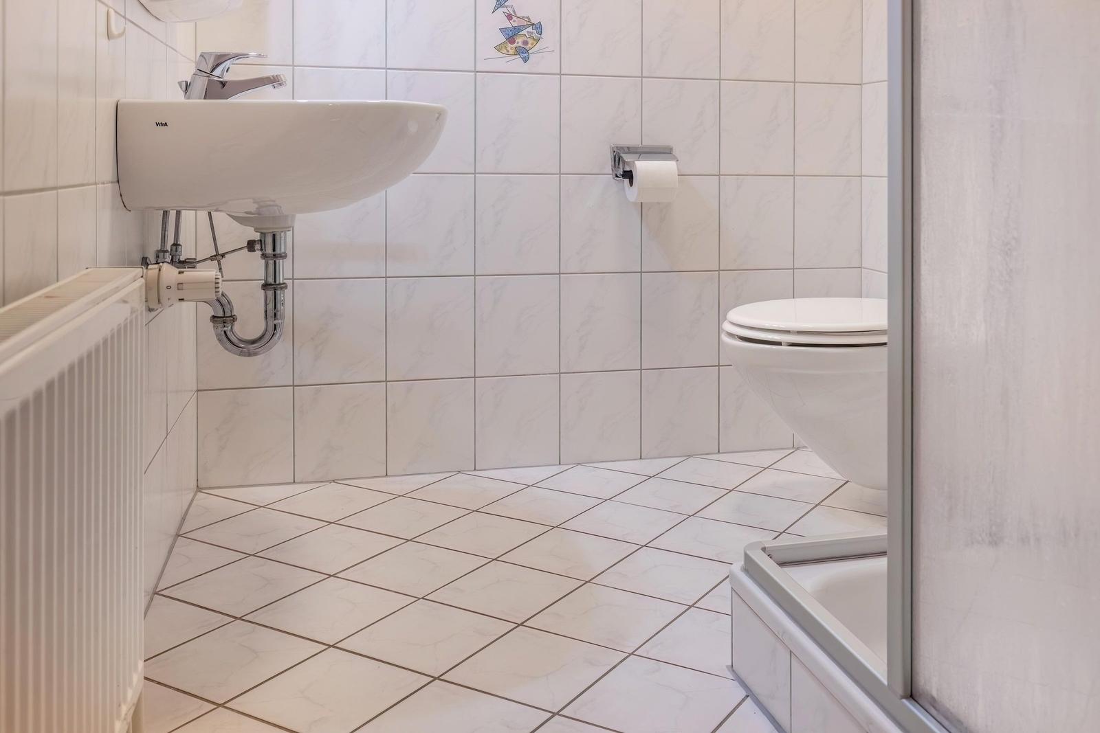 Badezimmer mit Waschbecken, Toilette und Dusche. Fliesenwand und Boden.