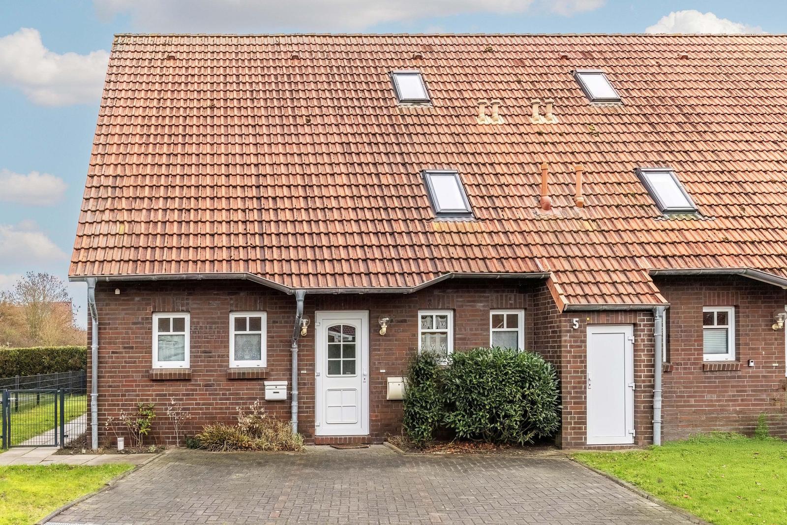 Ein Haus mit rotem Ziegeldach, weißen Türen und Fenstern sowie einem gepflasterten Vorplatz.