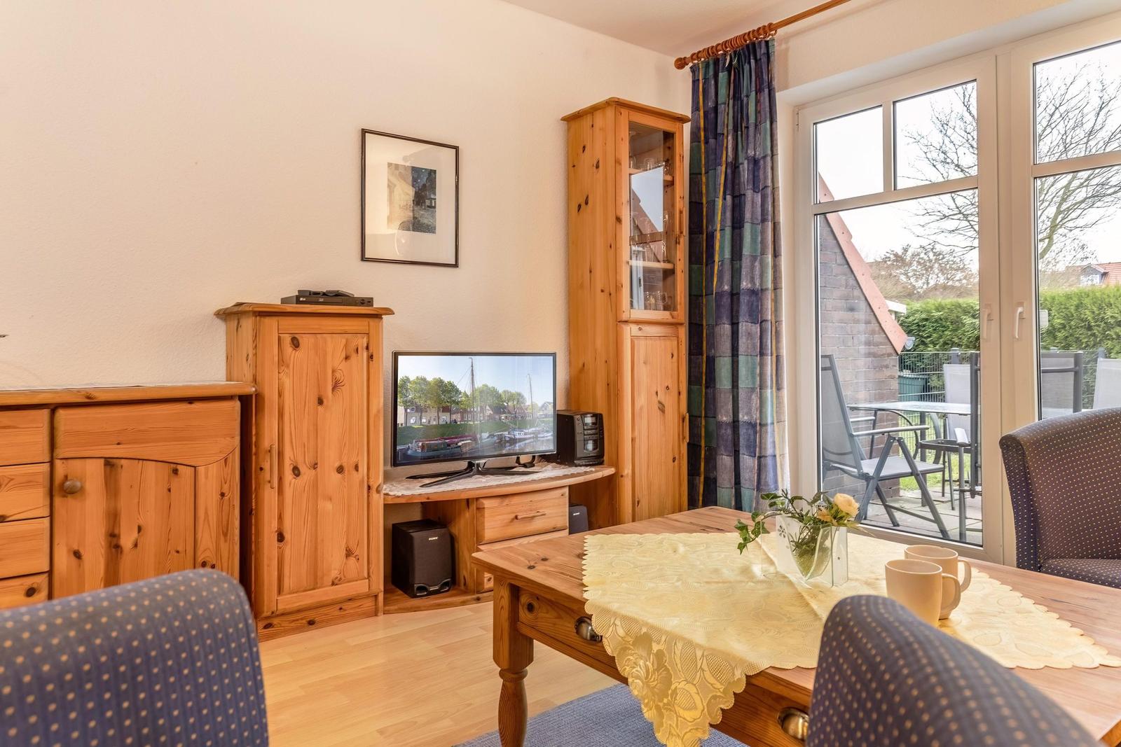 Wohnzimmer mit Holzmöbeln, Fernseher und Blick auf die Terrasse.