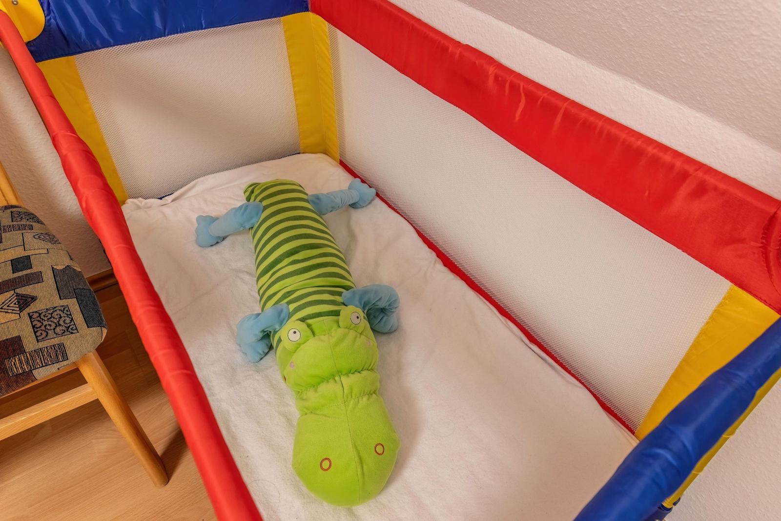Ein Kinderbett mit einem grünen Krokodil-Stofftier und einem weißen Laken.