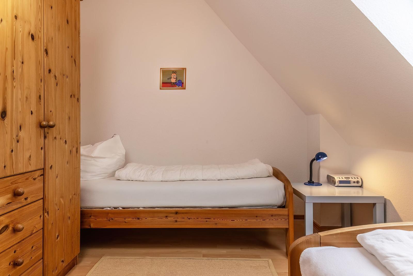 Ein Schlafzimmer mit Holzbett, Kleiderschrank und Nachttisch unter Dachschrägen.