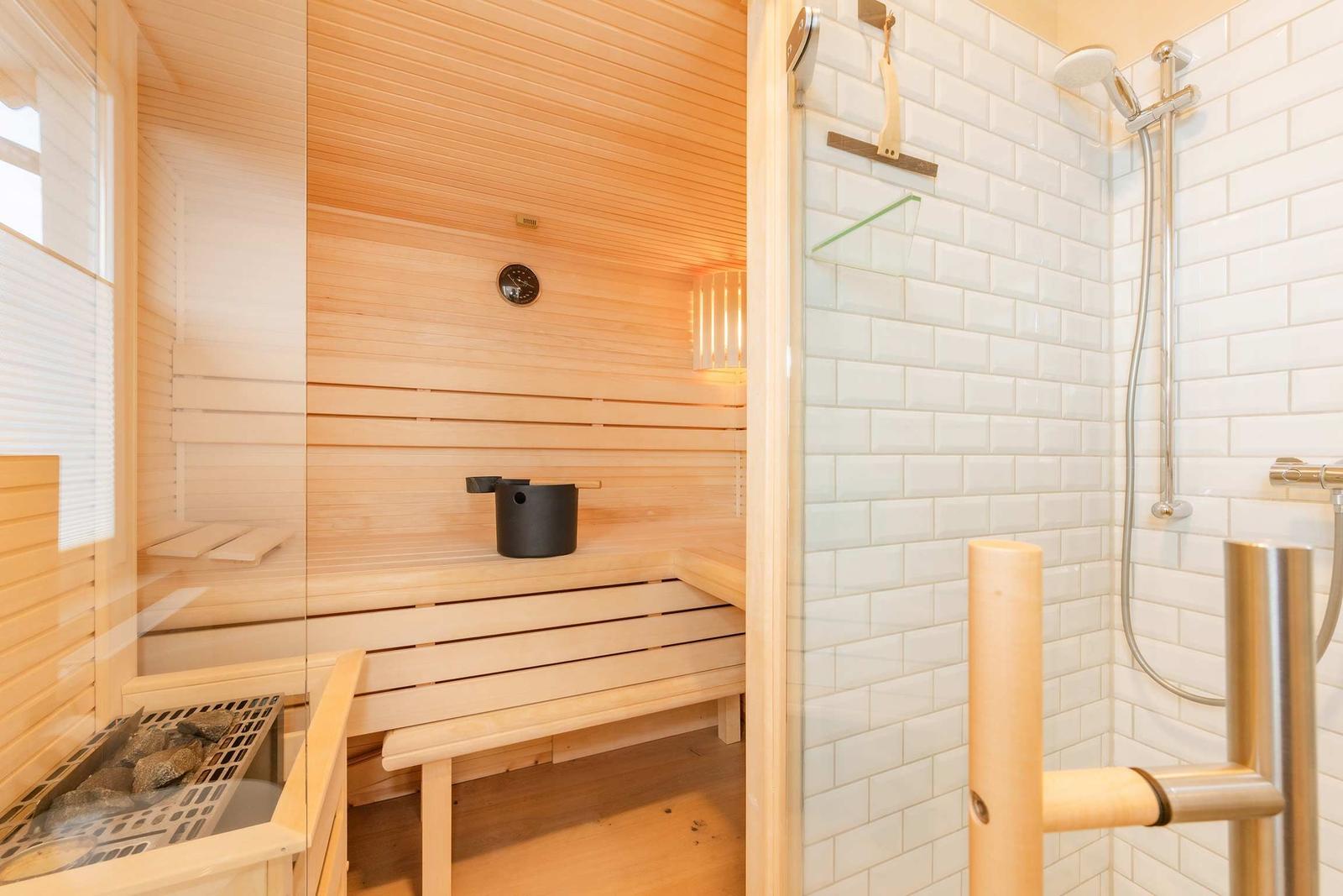 Sauna mit Holzbänken und Dusche mit Fliesenwand.