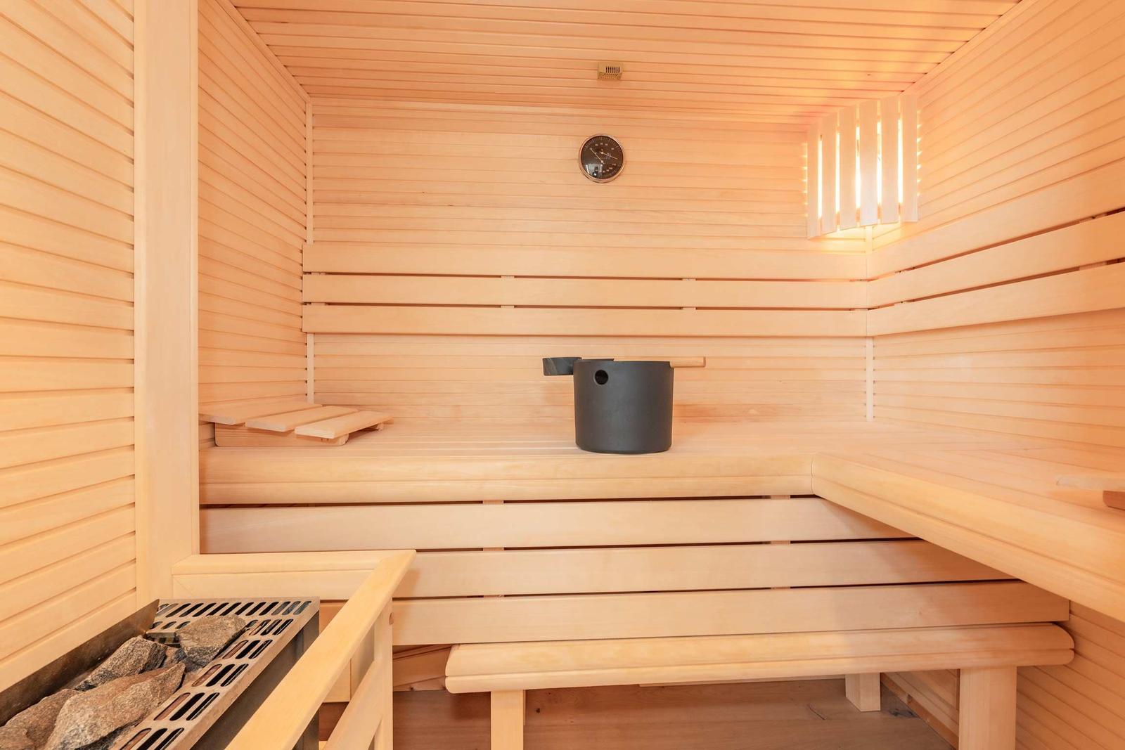 Sauna mit Holzbänken, Thermometer und schwarzer Schale.
