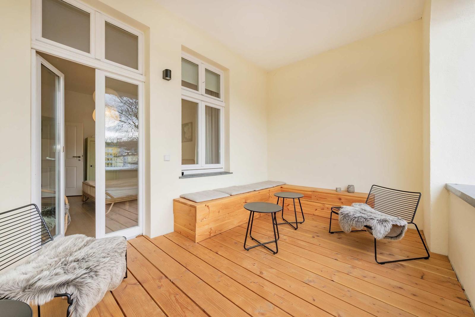 Terrasse mit Holzboden, Sitzbank, zwei Stühlen und Tischen. Durchgang ins Innere.