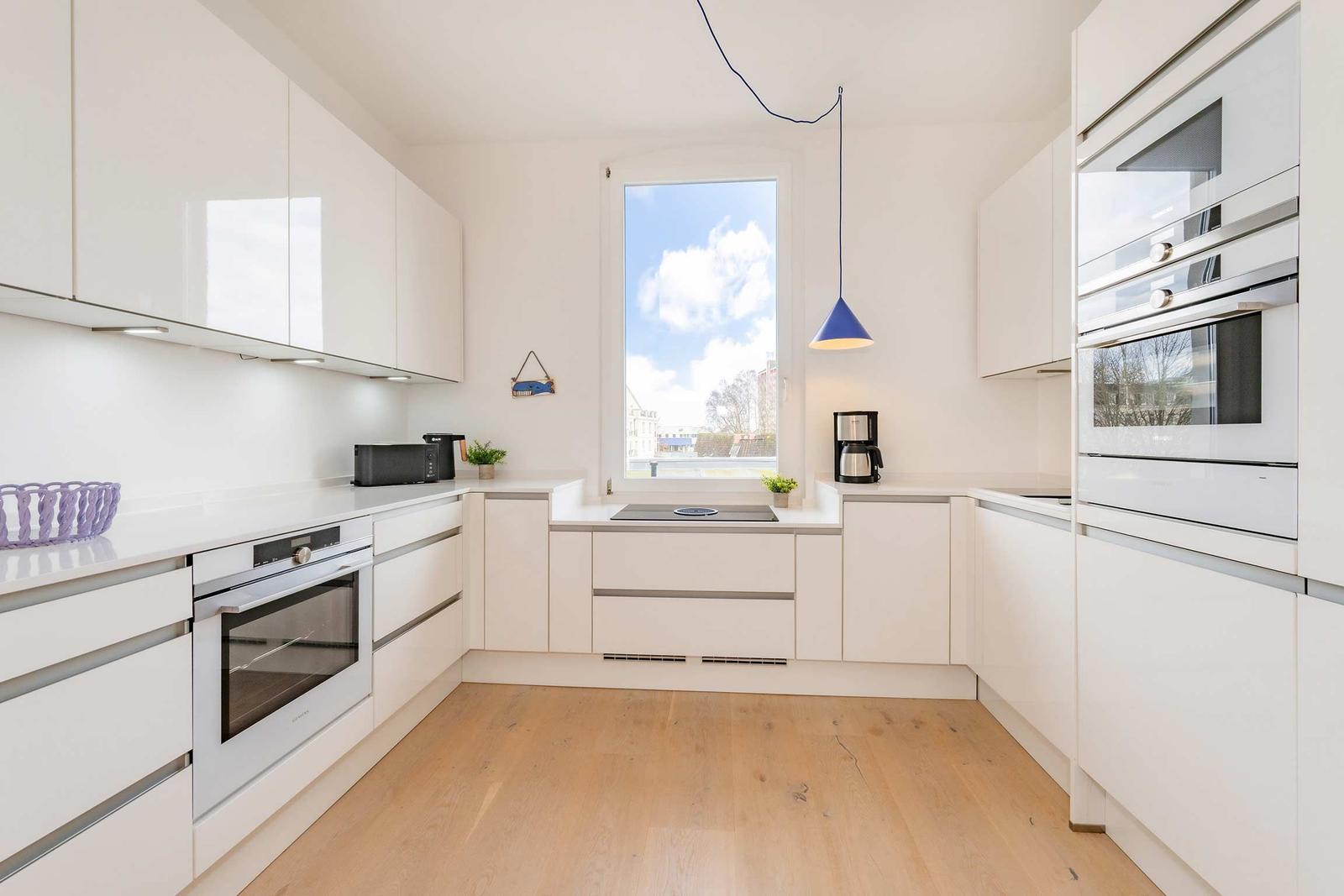 Moderne Küche mit weißen Schränken, Edelstahlgeräten und Holzboden.