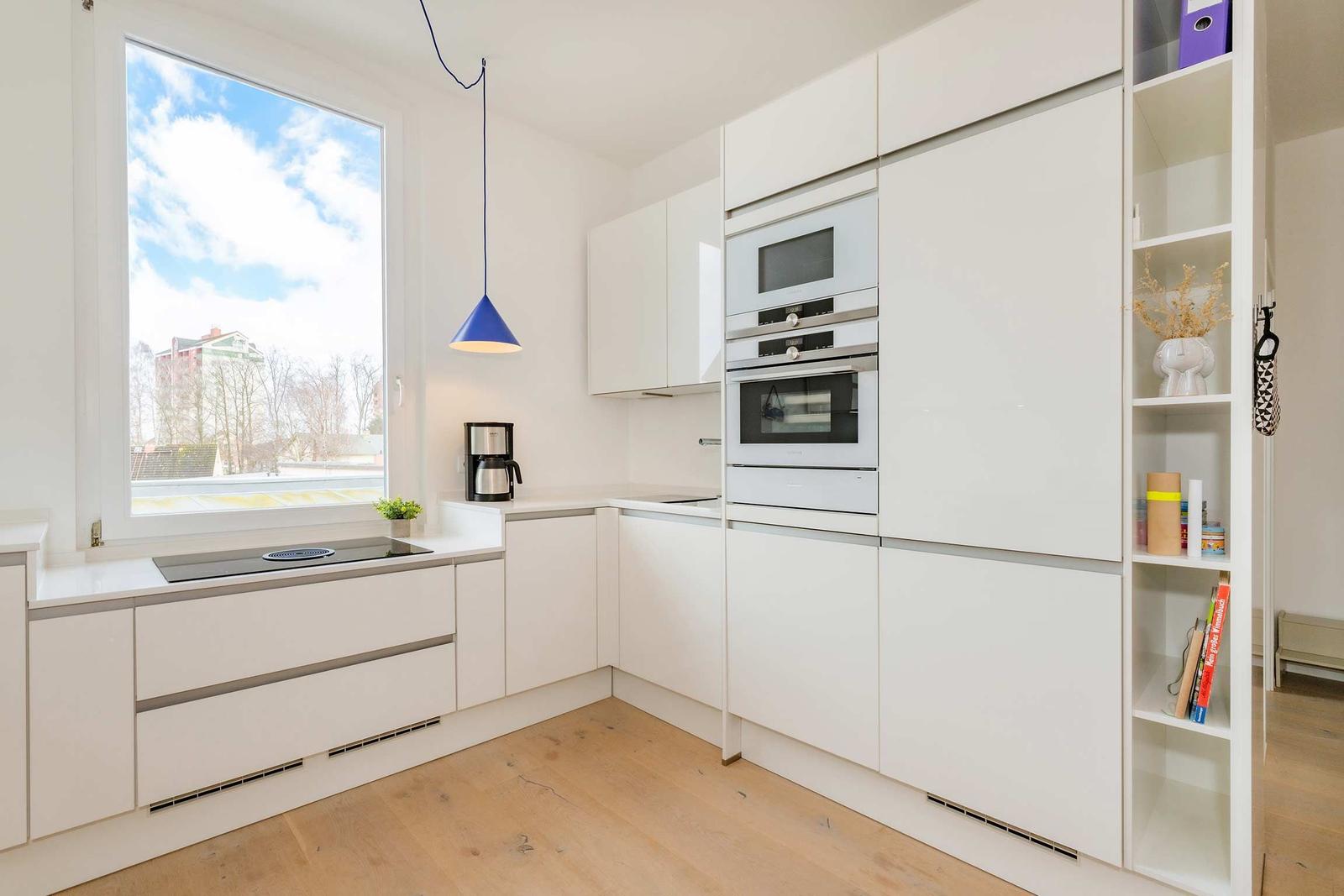 Küche mit weißen Schränken, integriertem Ofen und Fenster mit Blick nach draußen.