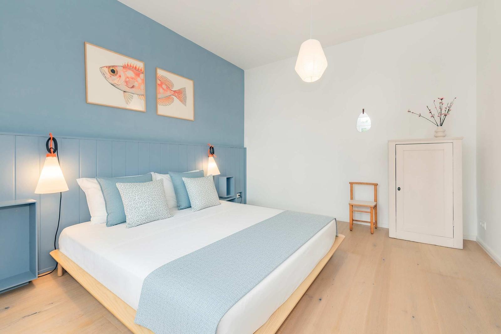Schlafzimmer mit Bett, Wandbildern und Holzboden.