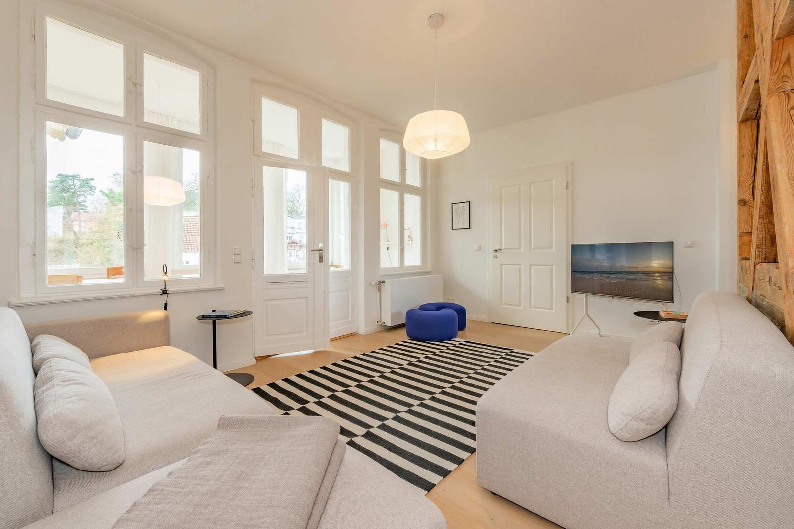 Wohnzimmer mit Sofa, Fernseher und großen Fenstern.