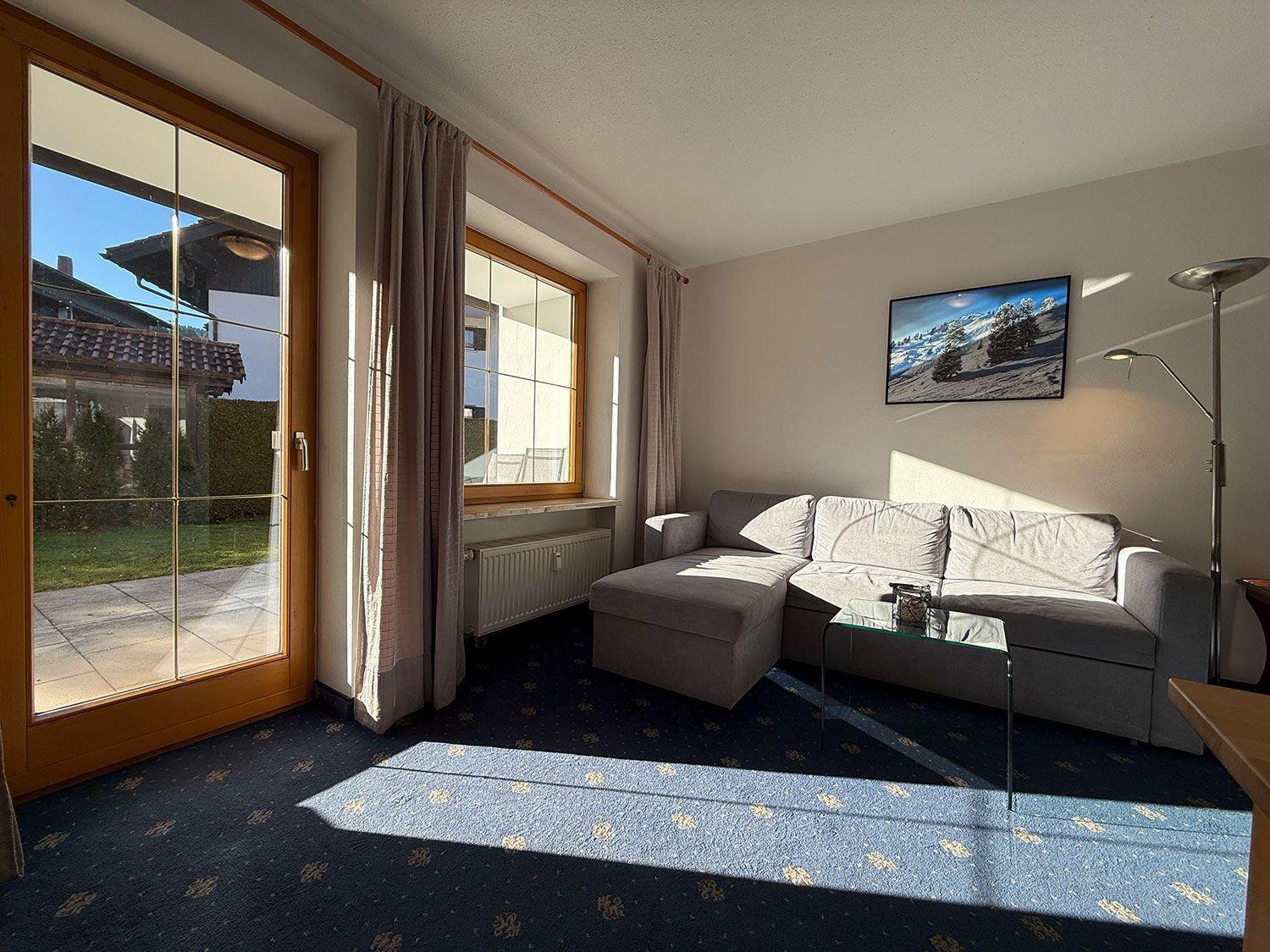 Wohnzimmer mit Sofa, Glas-Tisch und Blick auf den Garten.