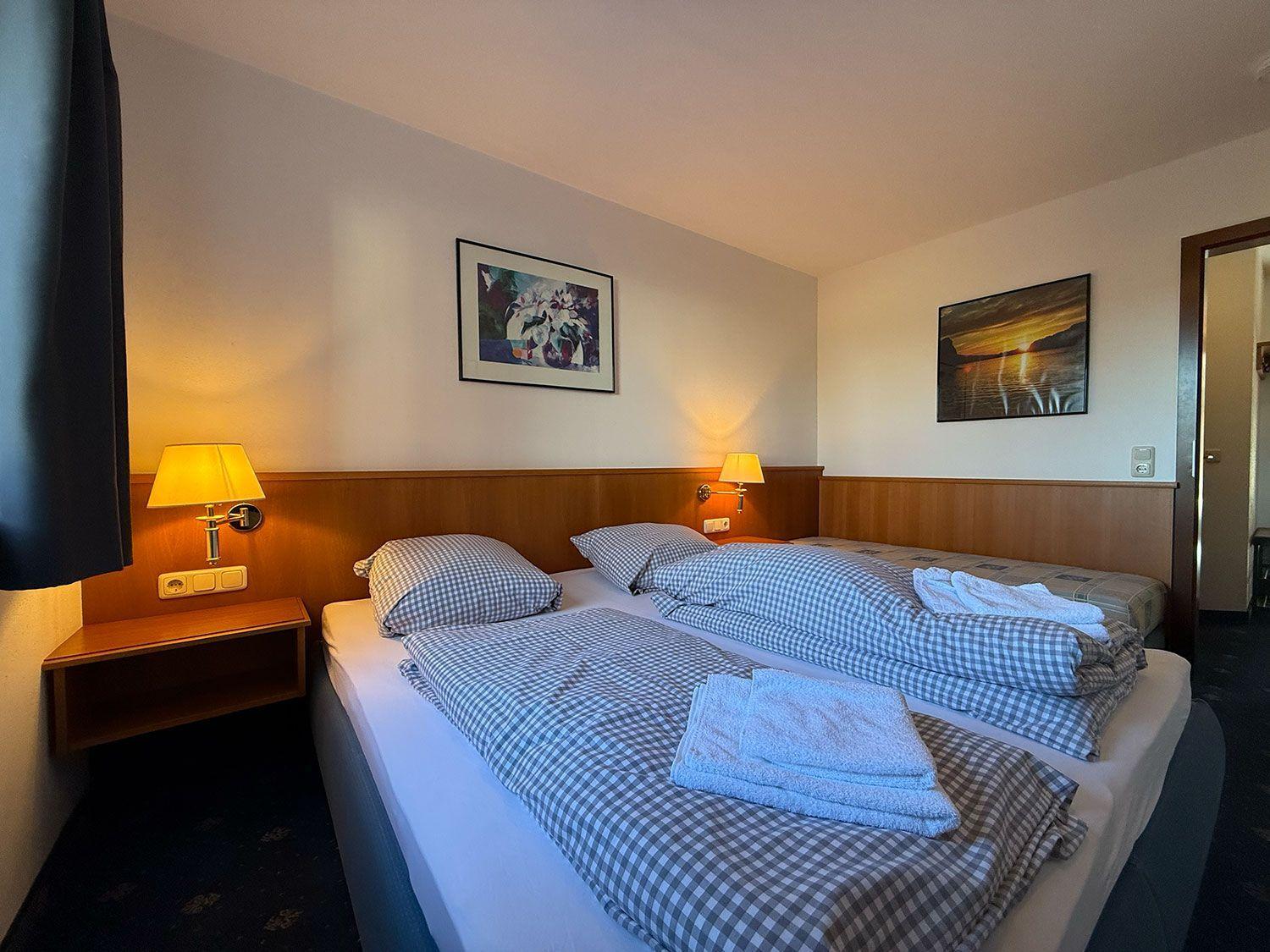 Zimmer mit Doppelbett, zwei Nachttischen und Wandbildern.