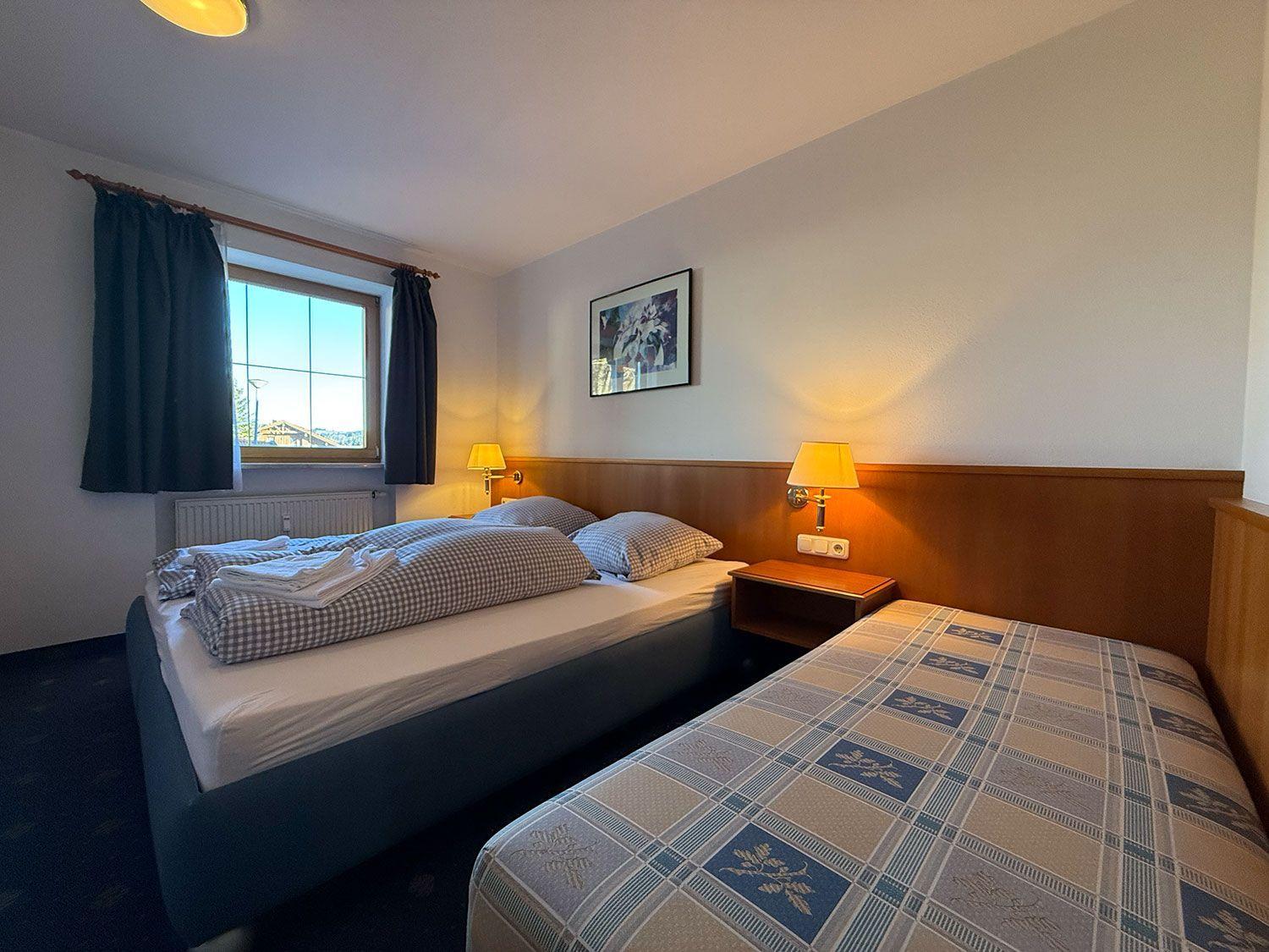 Zwei Betten mit Bettwäsche, Nachttische und Lampen. Fenster mit Vorhängen und Wandbild.