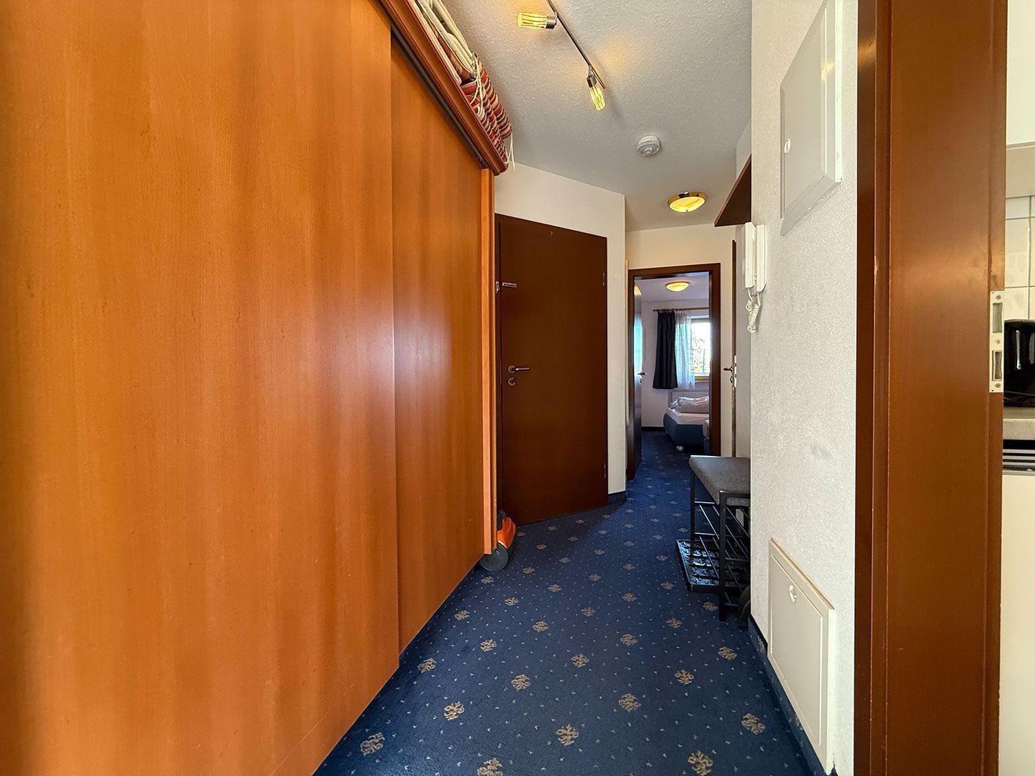 Flur mit Holzwand, blauem Teppich und Blick in Schlafzimmer.