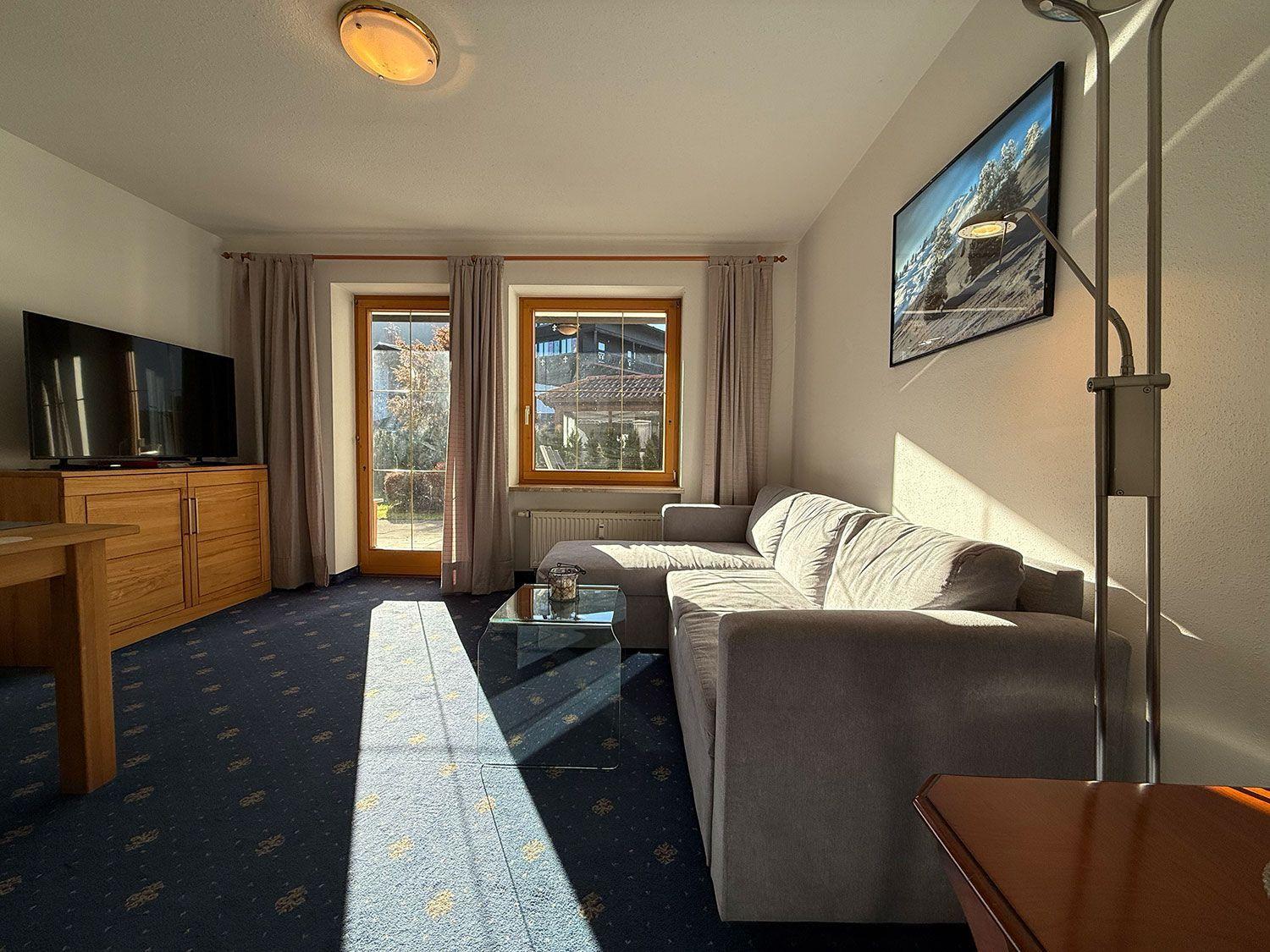 Wohnzimmer mit Sofa, Fernseher und Fenster zur Terrasse.