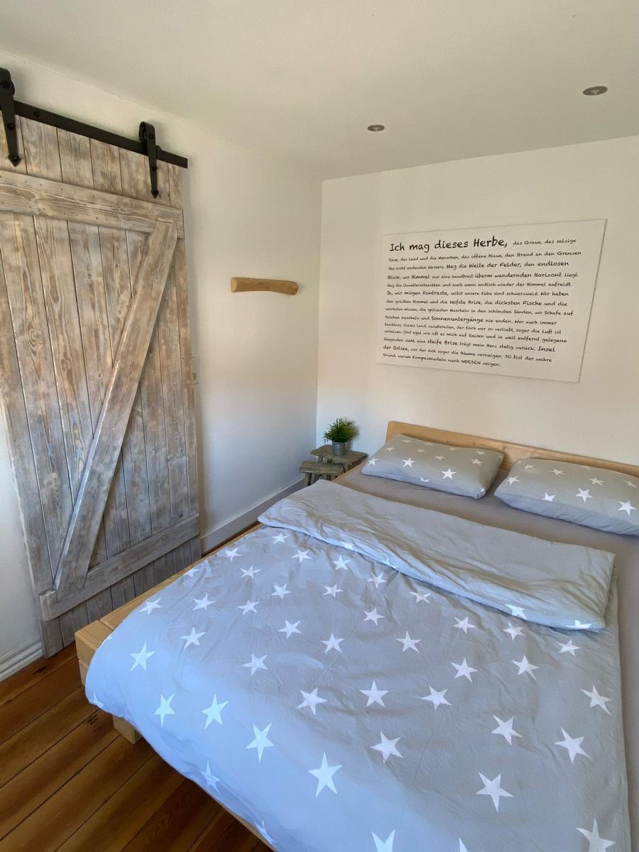 Schlafzimmer mit Bett, Holztür und Wandtext.